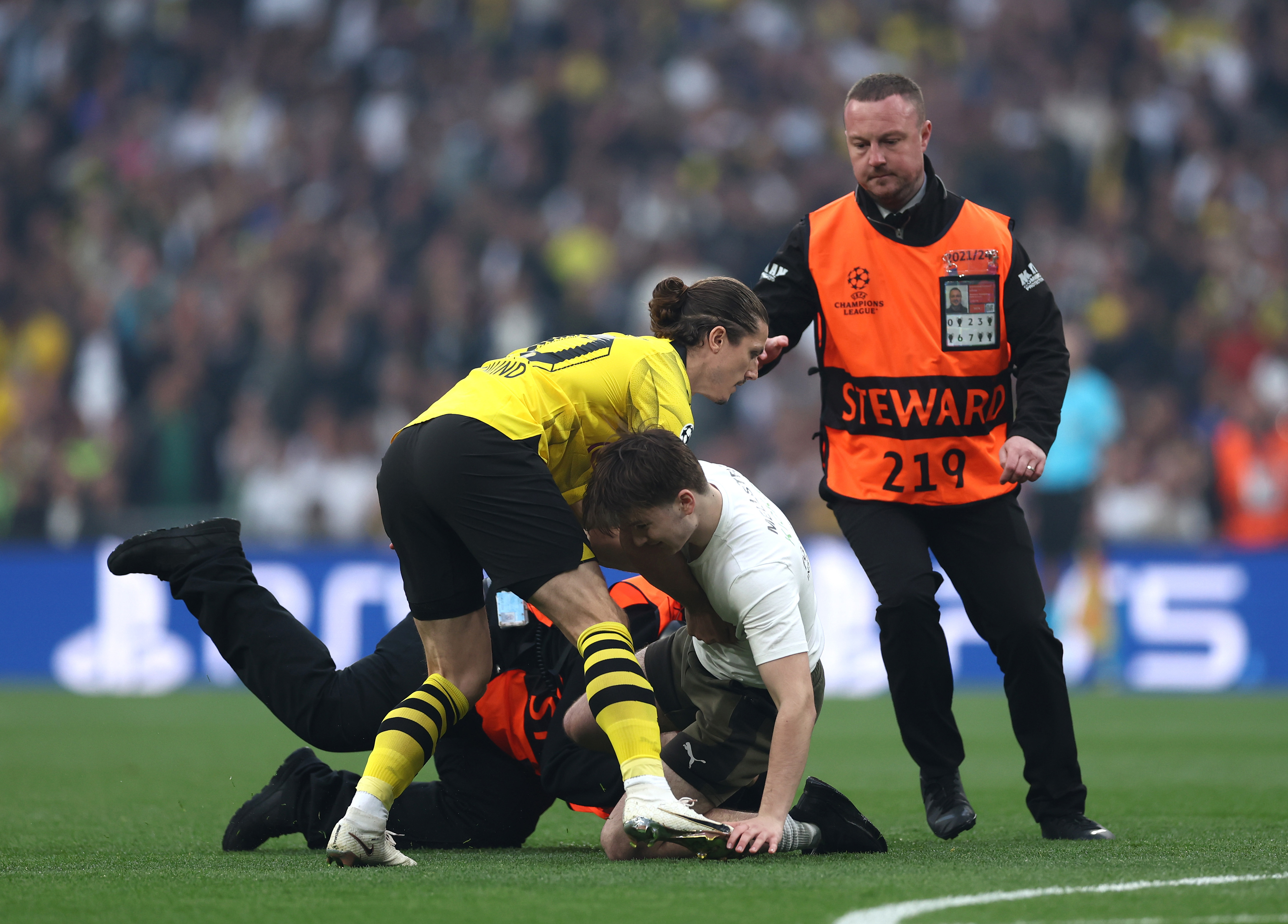 Marcel Sabitzer of Borussia Dortmund assists members of security as they stop a pitch invader.