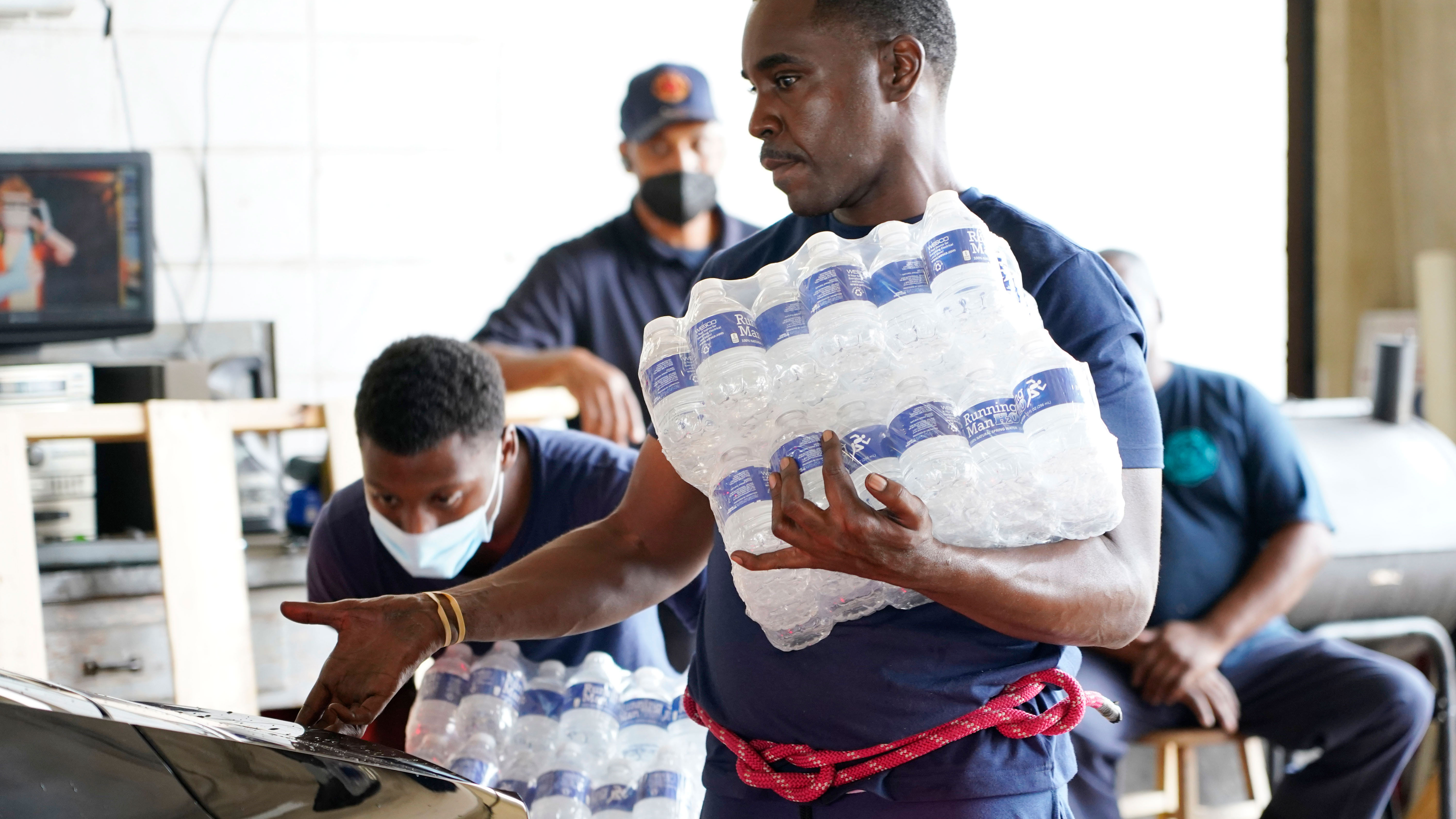 A recruit for the Jackson, Mississippi, Fire Department puts cases of bottled water in a resident's truck.