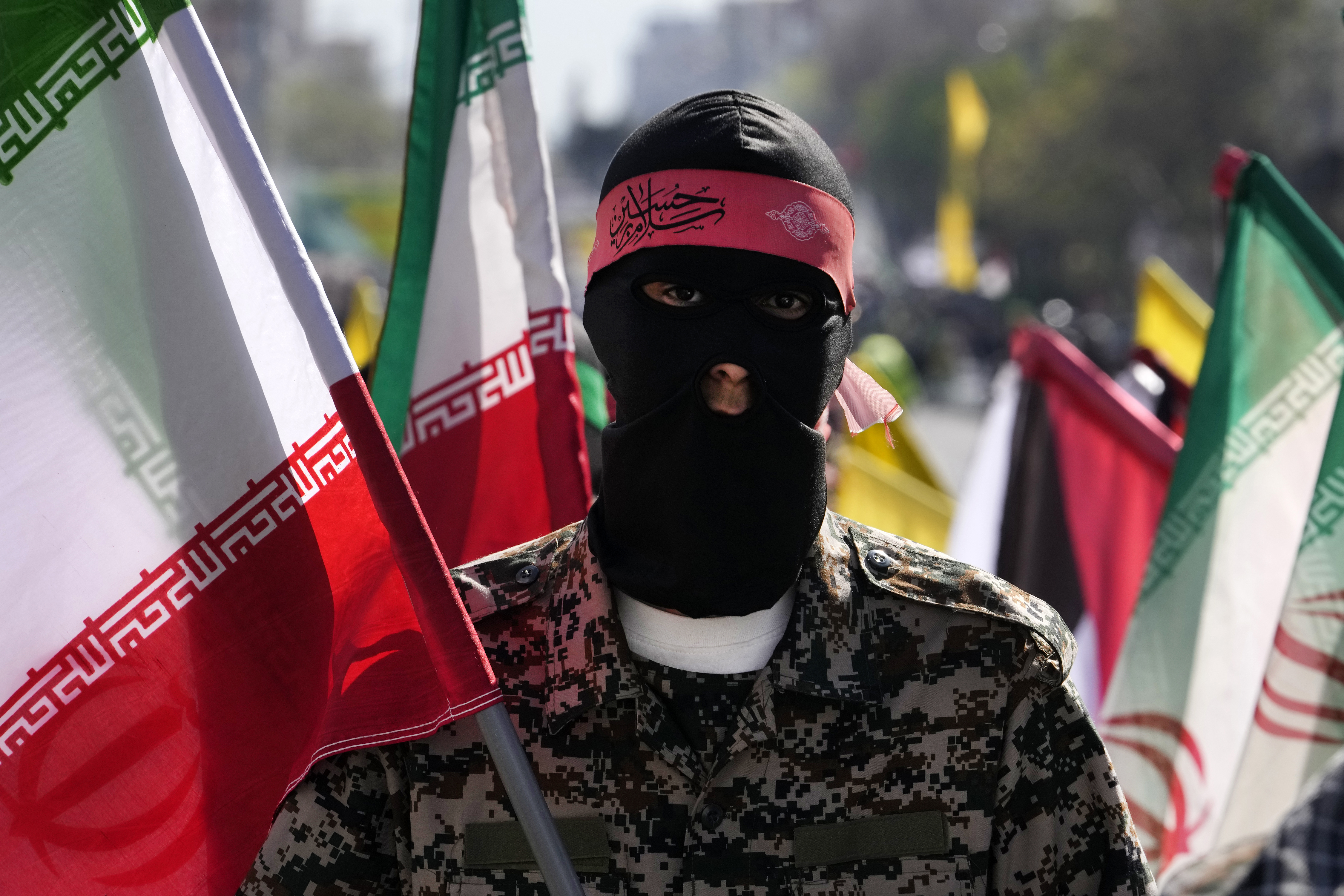 A member of the Iranian paramilitary Basij force holds an Iranian flag as he covers her face in the Palestinian and Lebanese militants style in an annual rally to mark Quds Day, or Jerusalem Day, to support the Palestinians in Tehran, Iran, Friday, April 5, 2024.