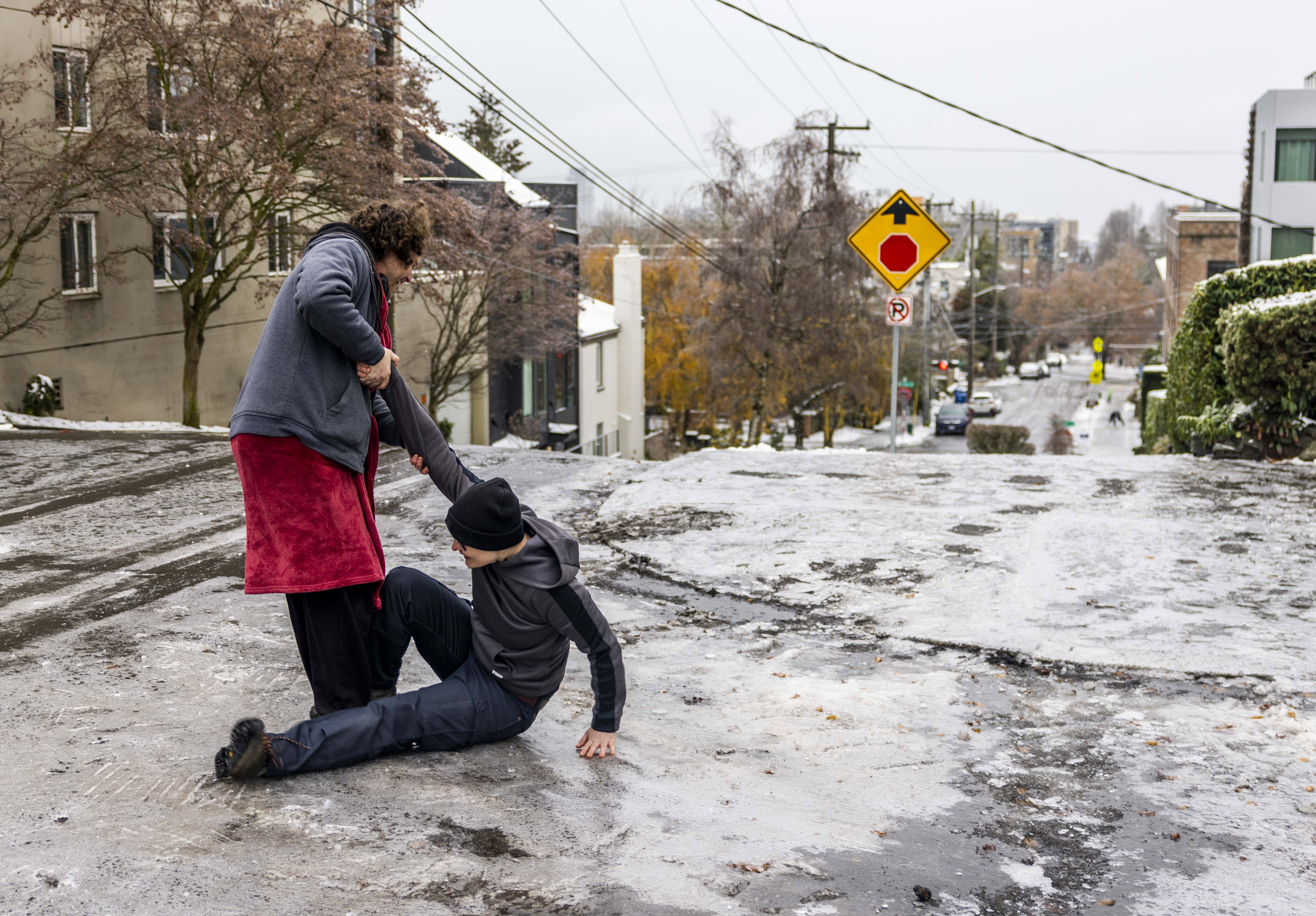 Garrett Fuller, left, helps friend Robin Jacobs get up after slipping to the icy ground on Capitol Hill, Friday, Dec. 23, 2022 in Seattle. 