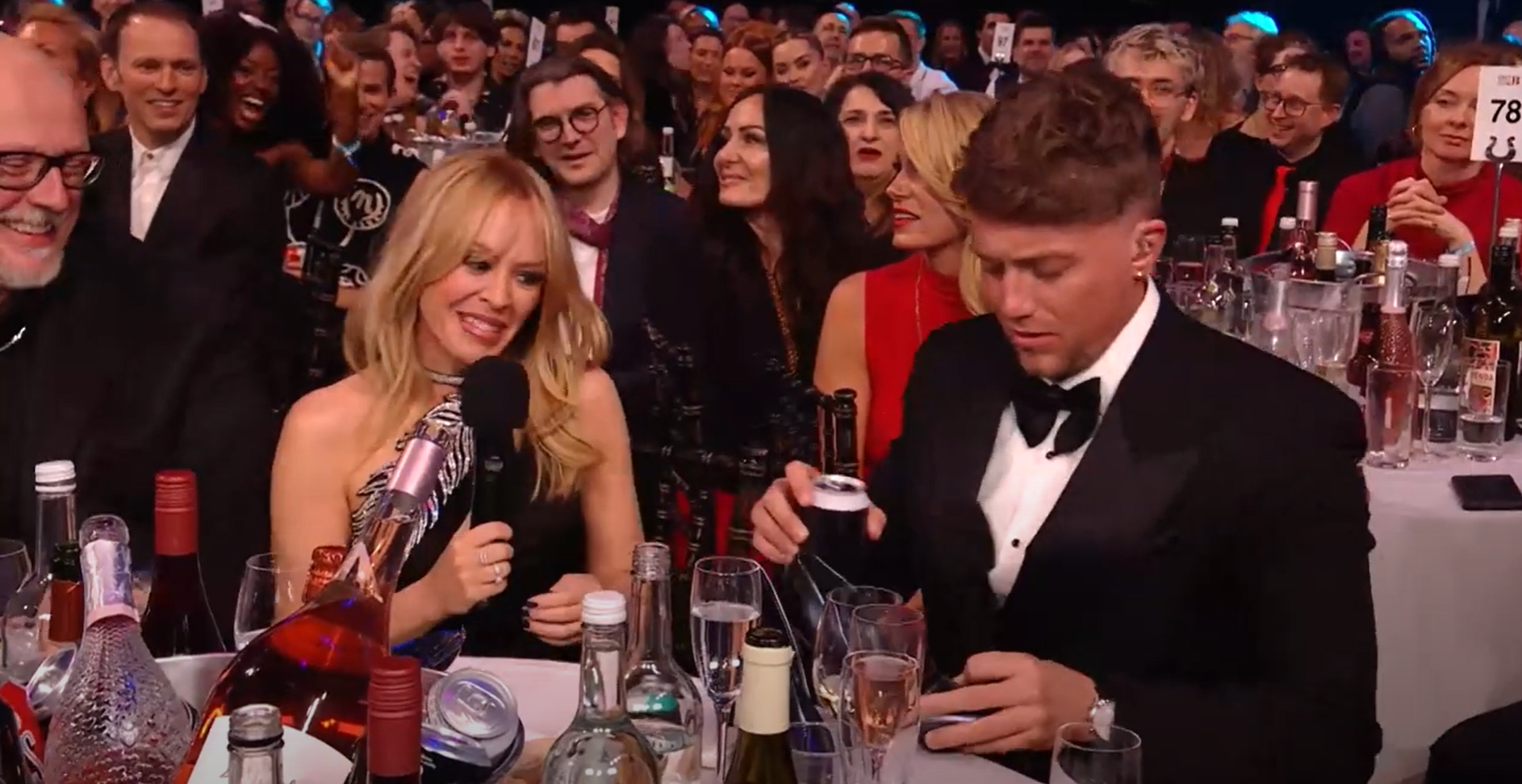 Kylie Minogue and Roman Kemp do a shoey during the 2024 Brit Awards