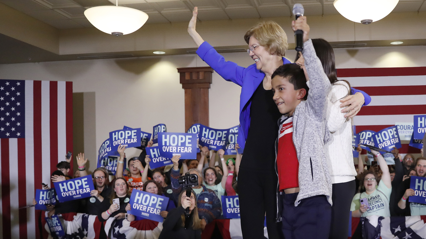 Elizabeth Warren stands on stage with her grandchildren as she arrives to speak at a caucus night rally the Forte Banquet and Conference Centre.