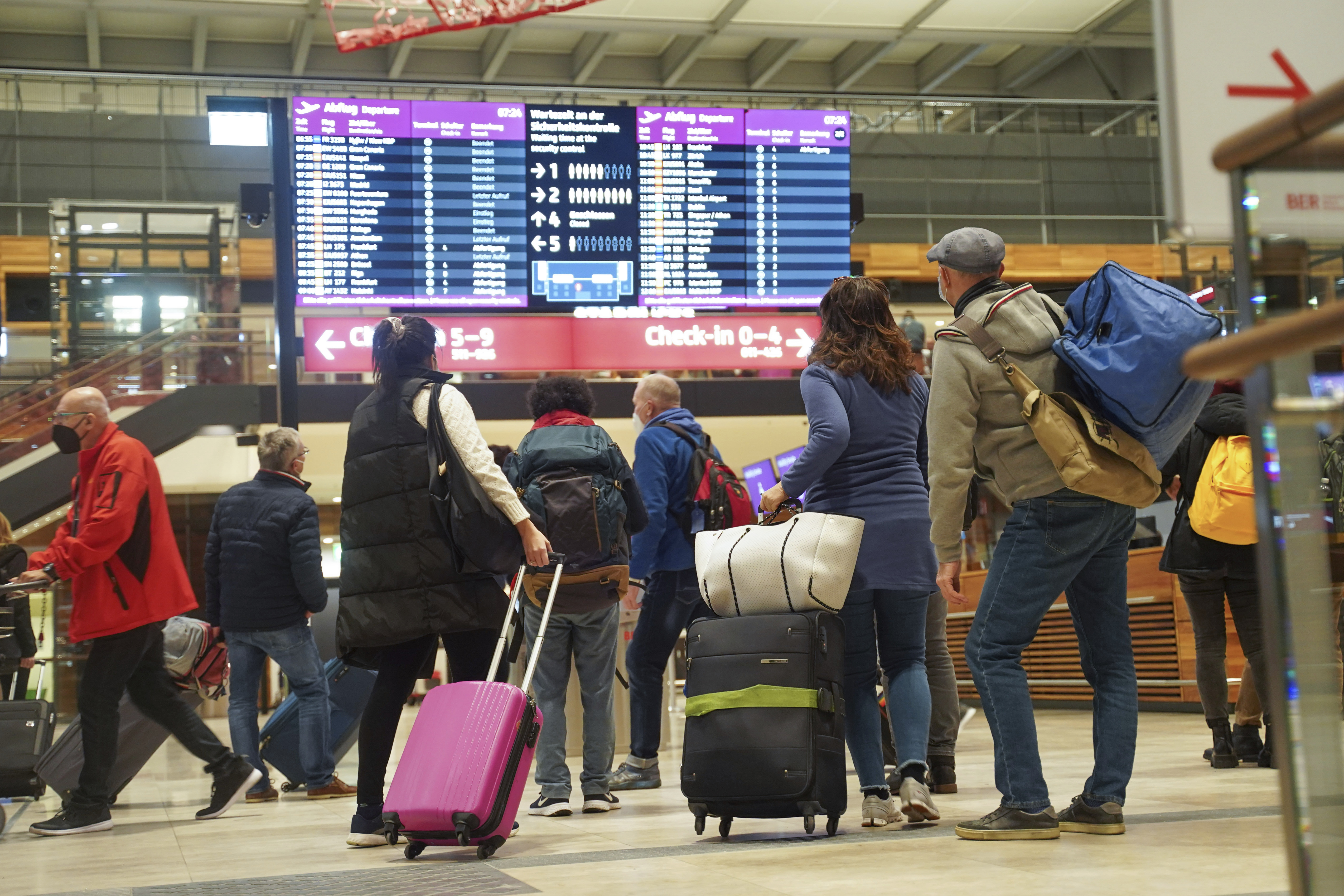 Travellers stand in front of an information board at BER Airport in Berlin, Germany, Saturday, Dec. 18, 2021. 