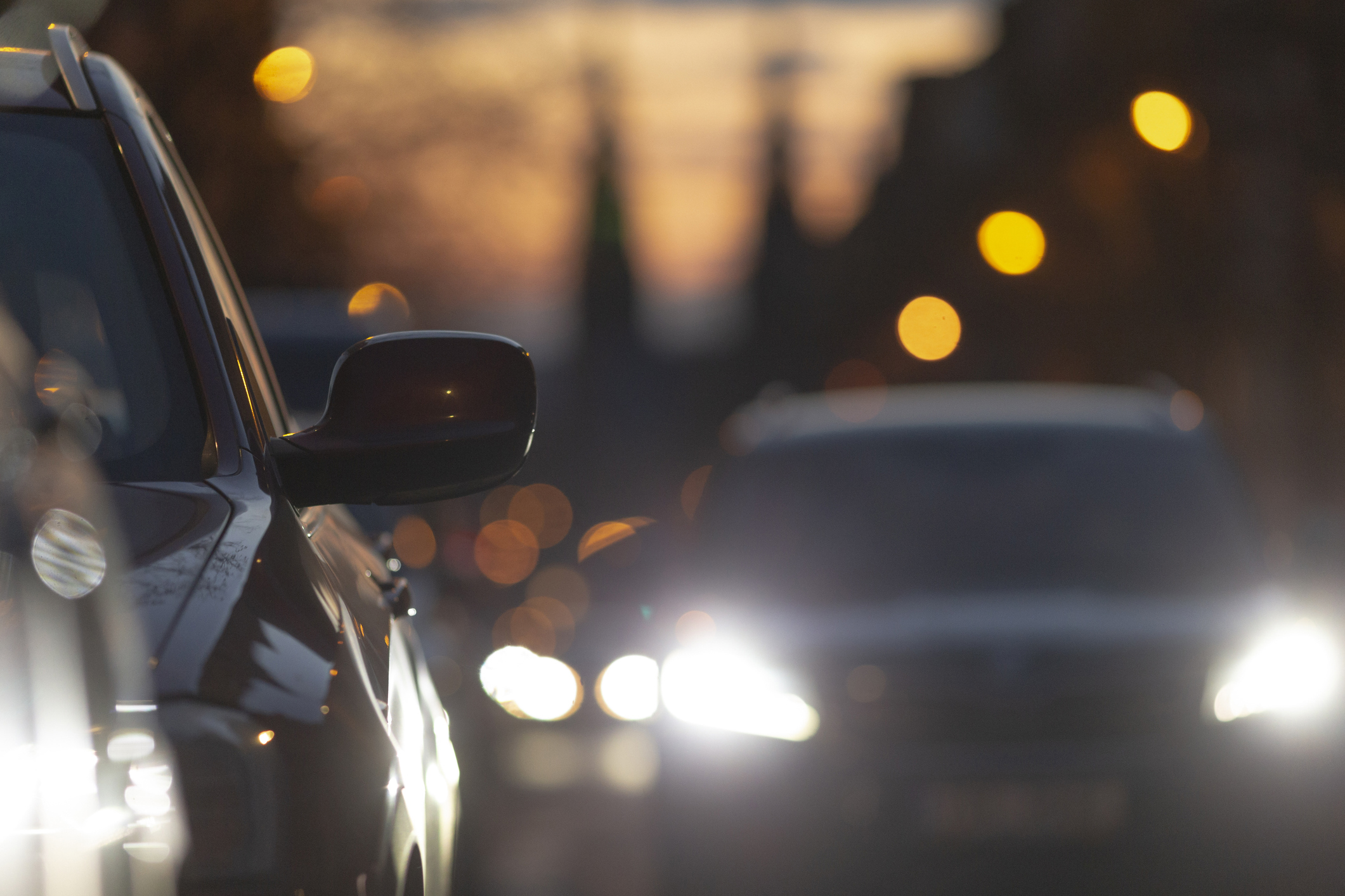 Cars in traffic during dusk, showcasing headlights and city lights, with a blurred background reflecting urban life