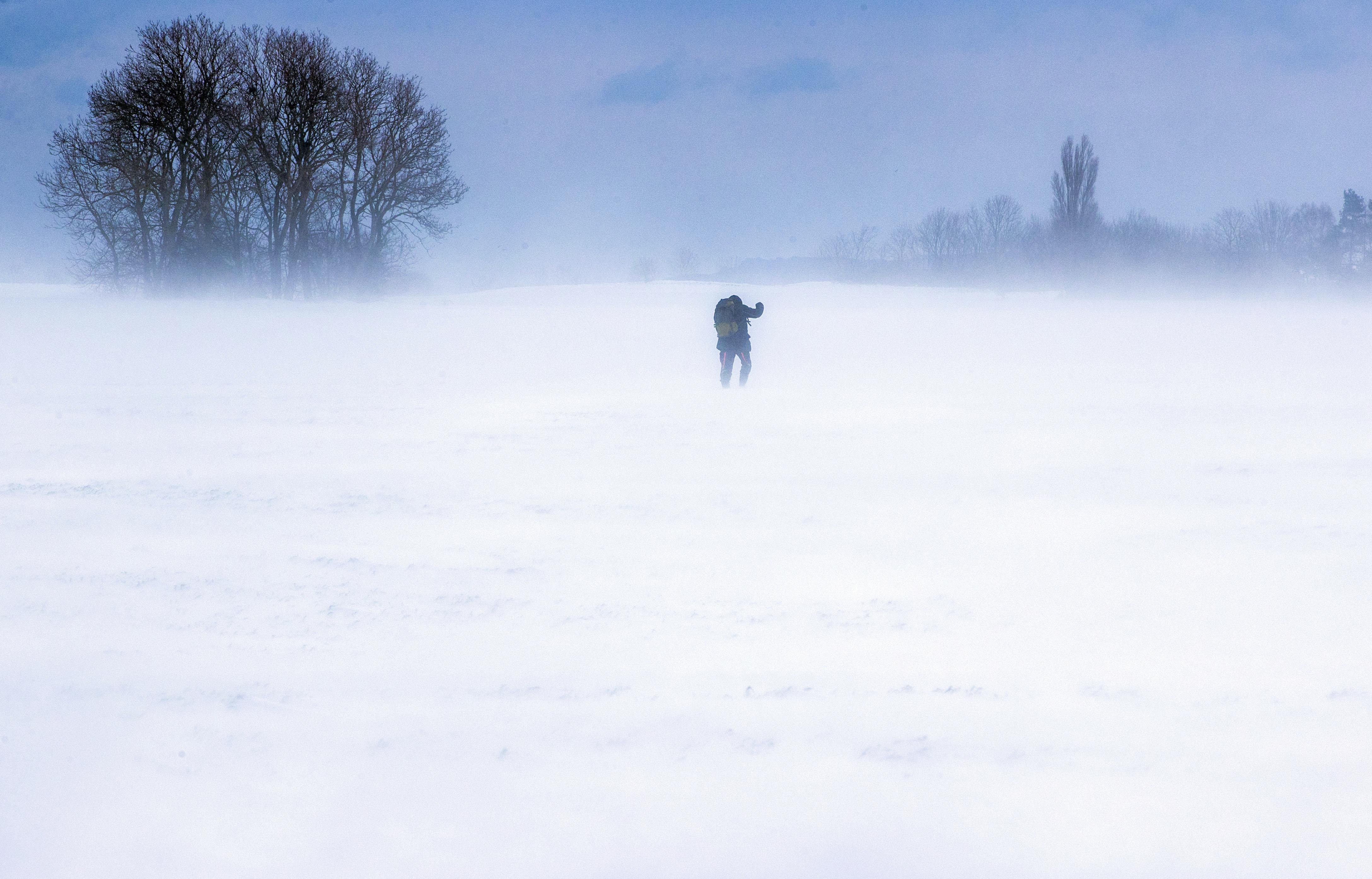 A man walks across a snow-covered field on the island of Ruegen, Germany, Sunday, Feb. 7, 2021. Strong winds are causing snow drifts in the north of the island. The German Weather Service (DWD) expects snowstorms and permafrost for northern Germany this weekend. (Jens Buettner/dpa via AP)