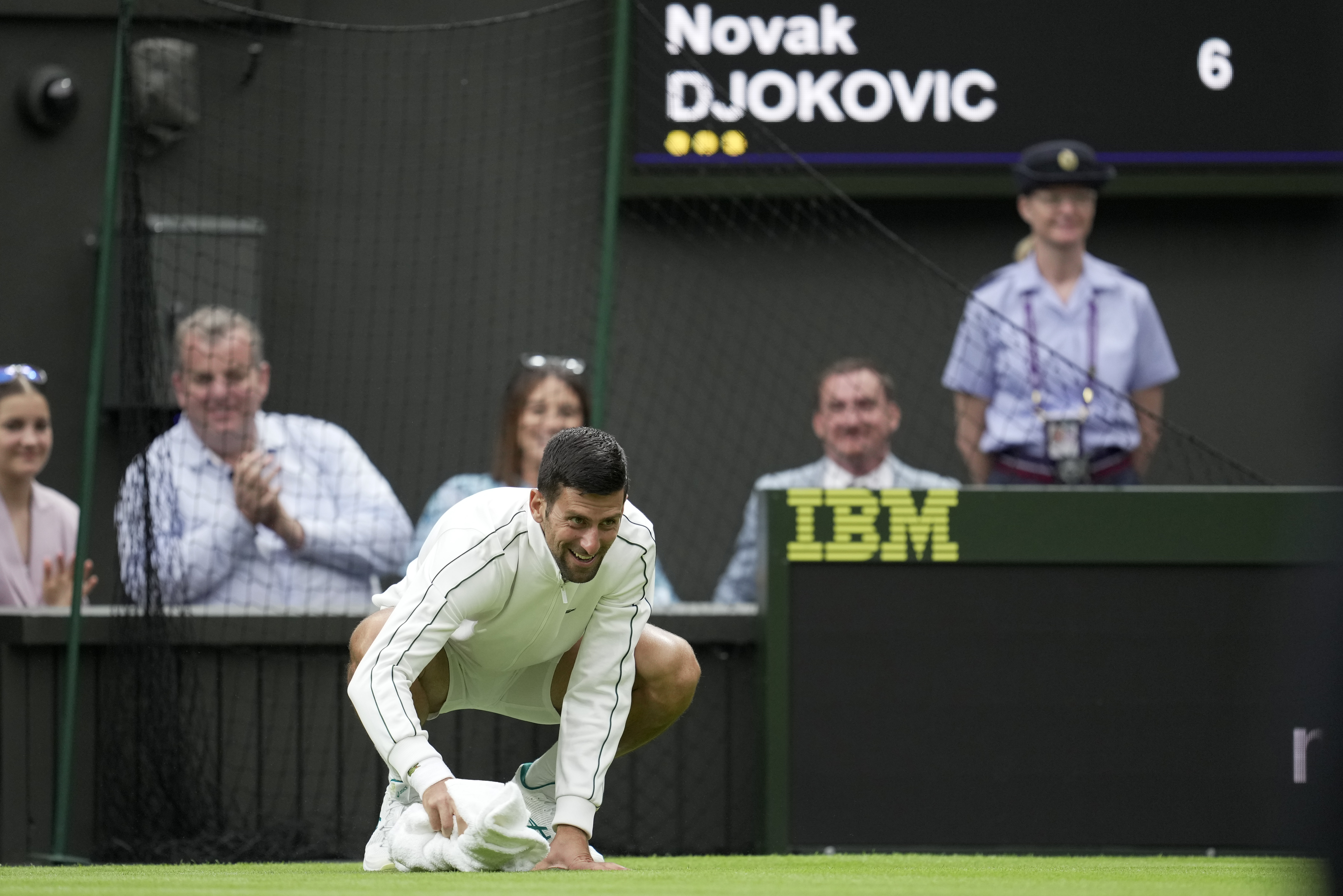 Novak Djokovic wipes the court with his towel after rain fell on day one, much to the amusement of courtside fans.