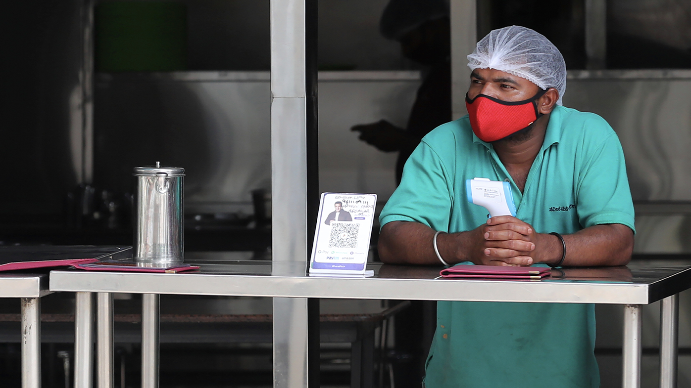 An eatery staff wearing a face mask as a precaution against coronavirus holds a thermometer as he waits to serve takeaway food to customers during lockdown in Bengaluru, India, Sunday, July 5, 2020. India's coronavirus caseload is fourth in the world behind the U.S., Brazil and Russia. (AP Photo/Aijaz Rahi)