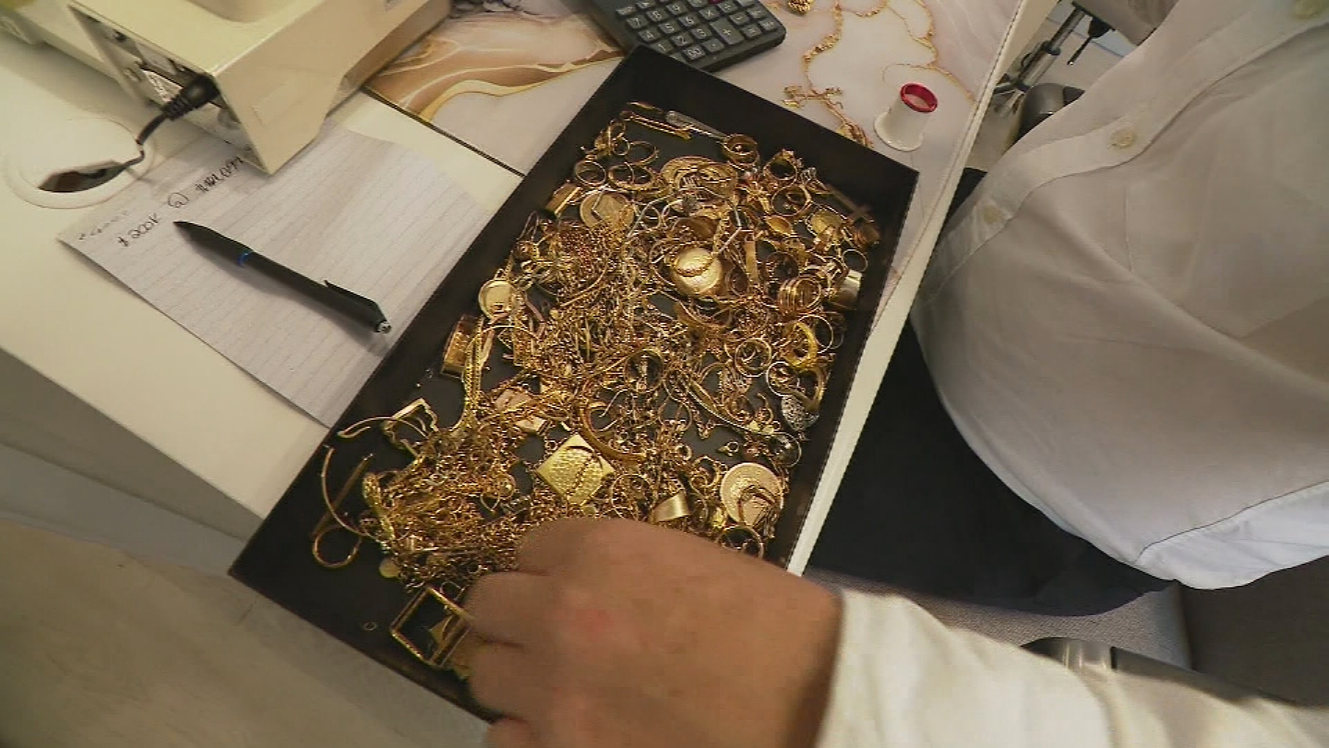 A box full of gold jewellery in a box on a white desk. 