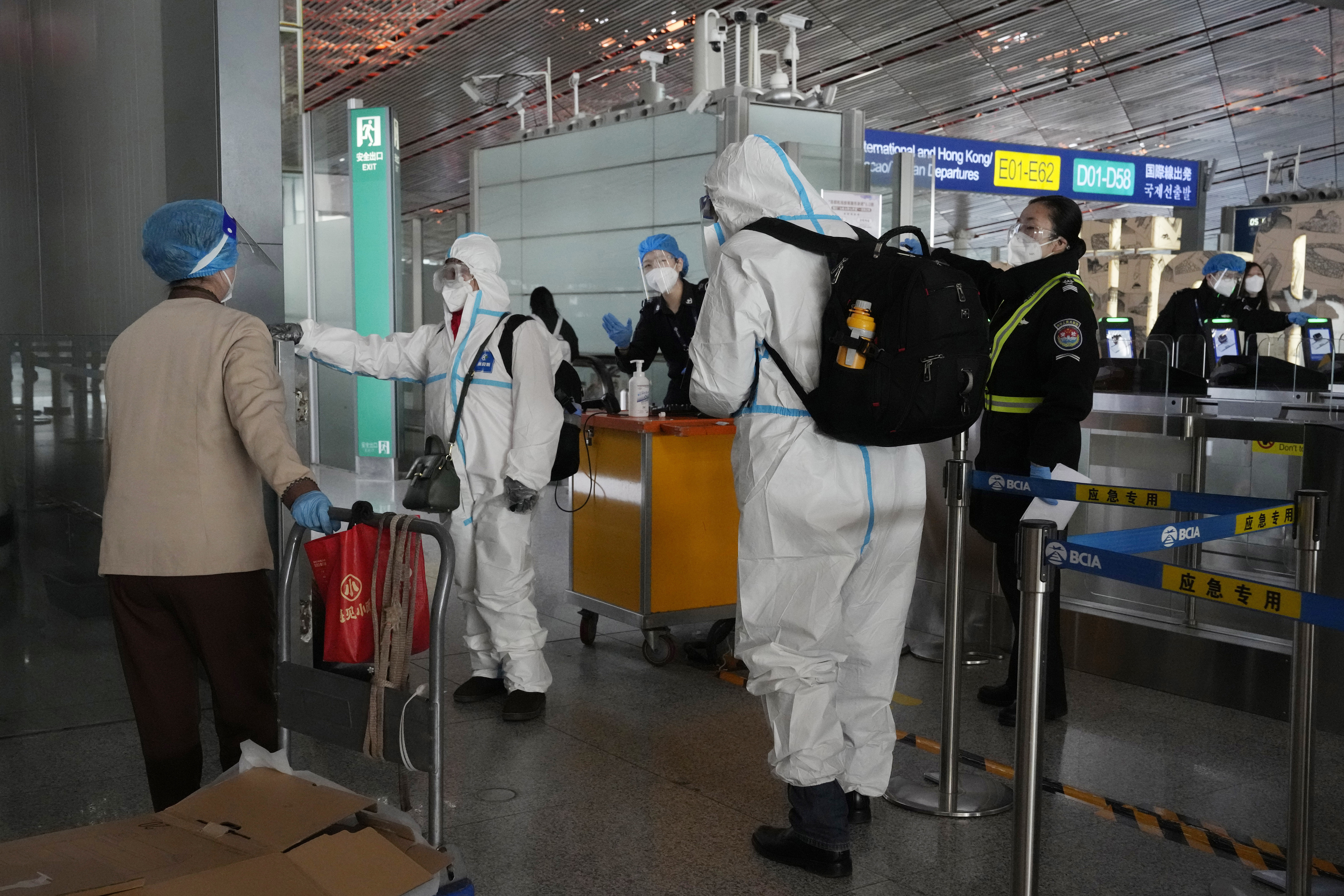 Passengers in protective gear are directed to a flight at a Capital airport terminal in Beijing, Tuesday, Dec. 13, 2022. Some Chinese universities say they will allow students to finish the semester from home in hopes of reducing the potential of a bigger COVID-19 outbreak during the January Lunar New Year travel rush.