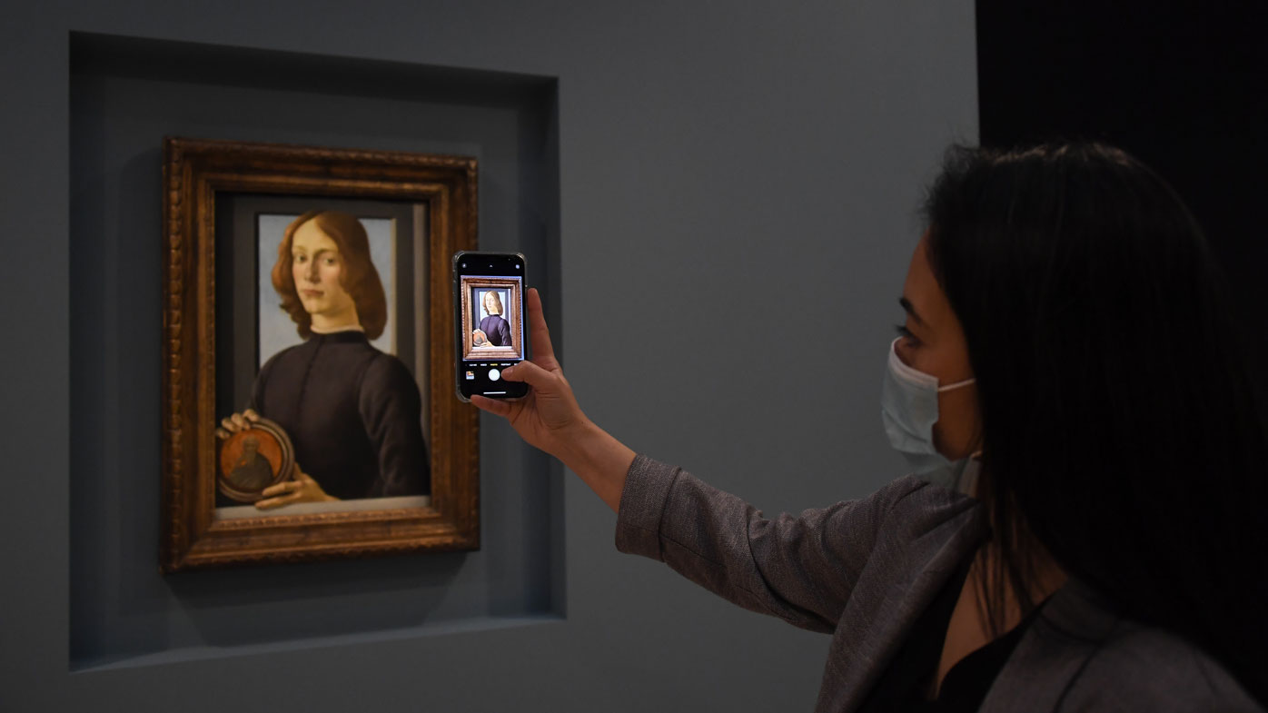A member of the staff takes a phone picture of the painting 'Young Man Holding a Roundel' by the Italian Renaissance painter Sandro Botticelli at Sotheby's, in London, Wednesday, Dec. 2, 2020