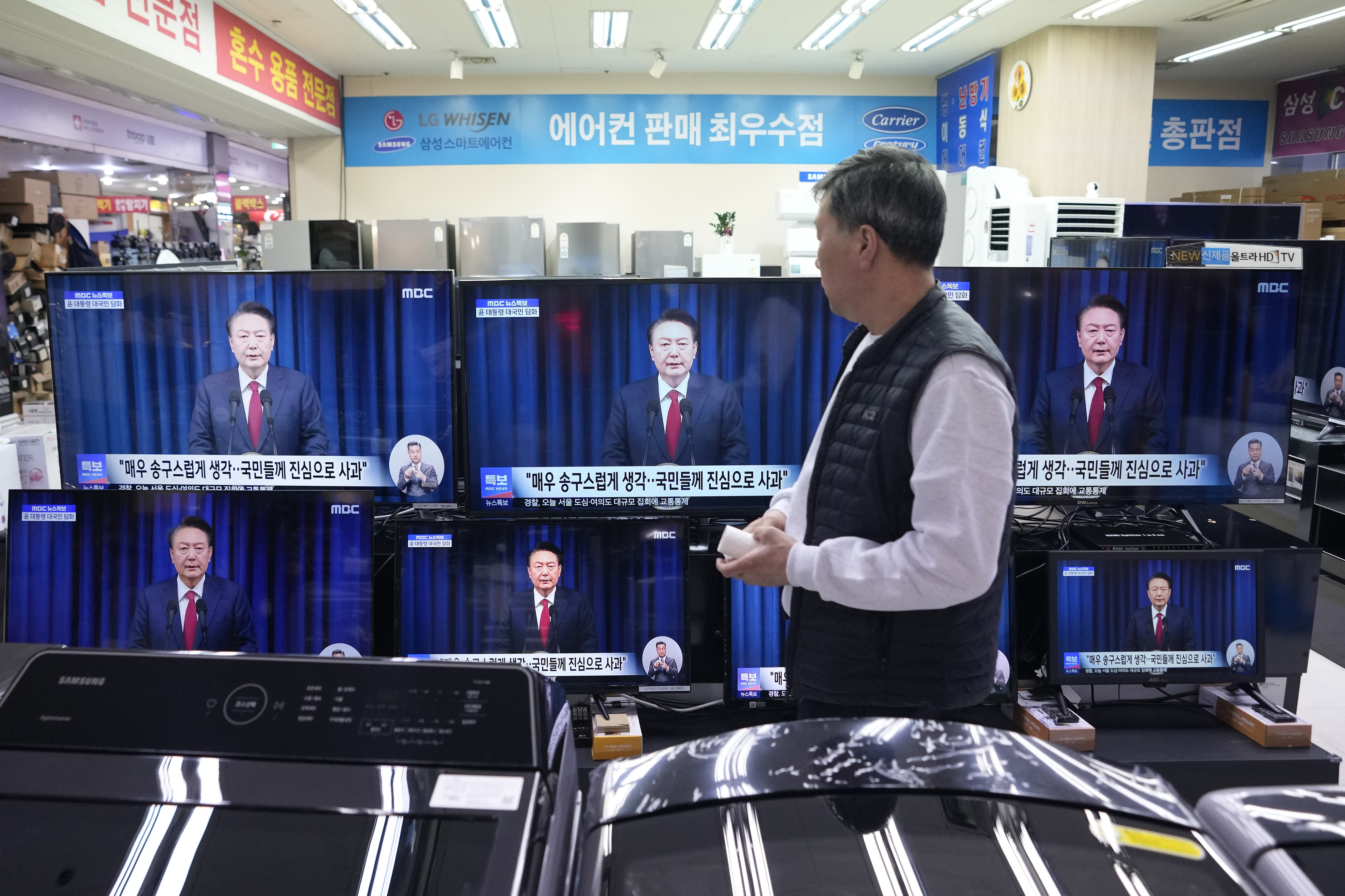 A man watches TV screens showing the broadcast of South Korean President Yoon Suk Yeol