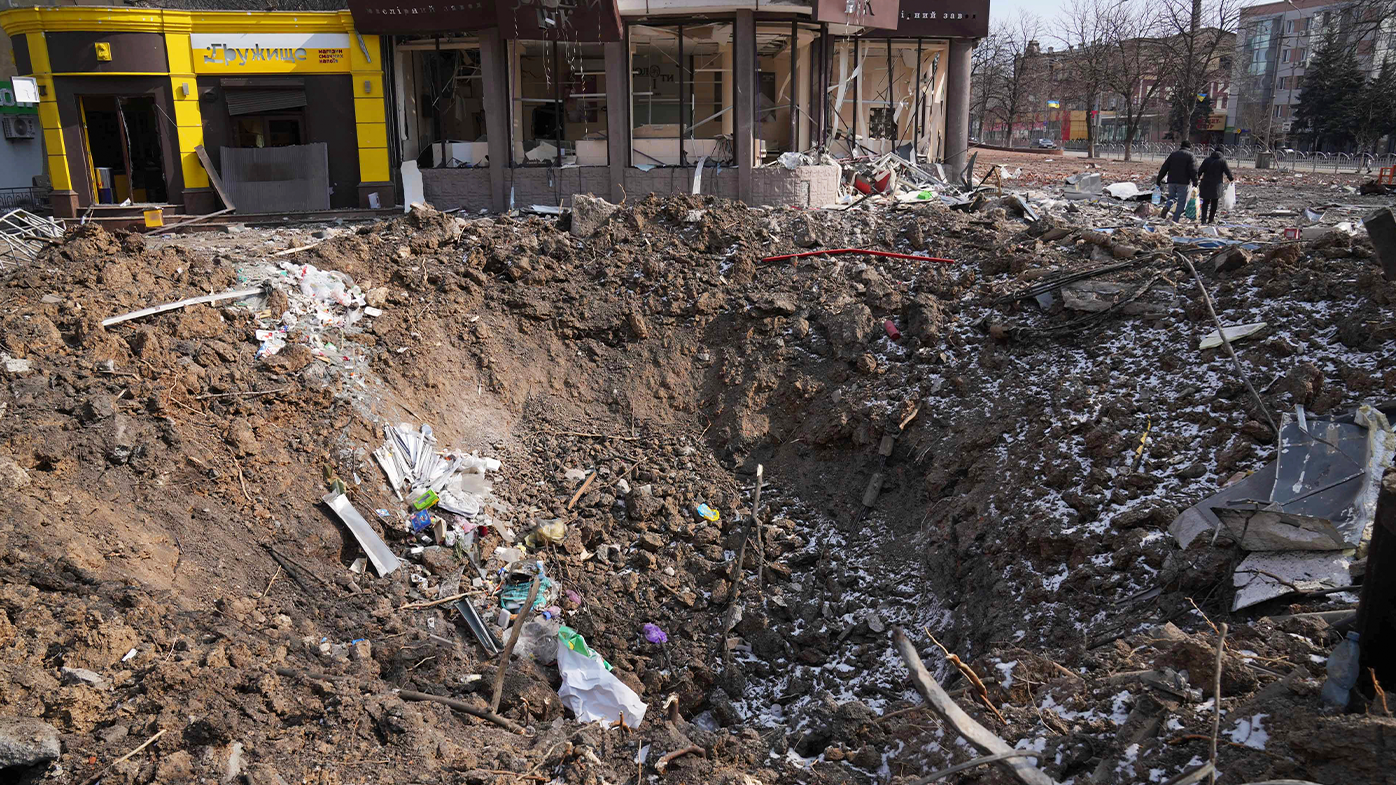  People walk past a crater from the explosion in Mira Avenue (Avenue of Peace) in Mariupol, Ukraine, Sunday, March 13, 2022. 