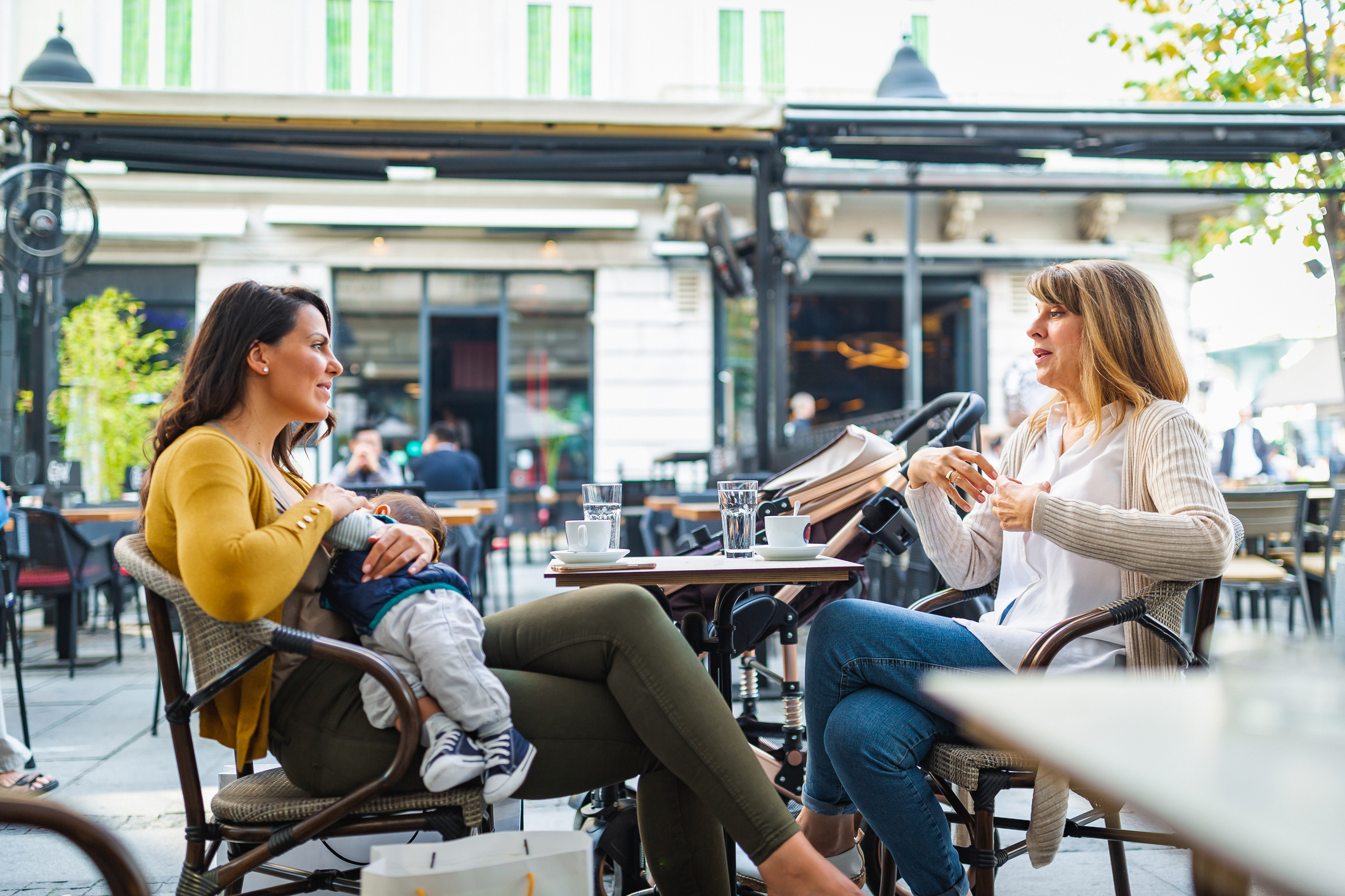 Young mother breastfeeding her baby boy in public while sitting in a cafe with her mother