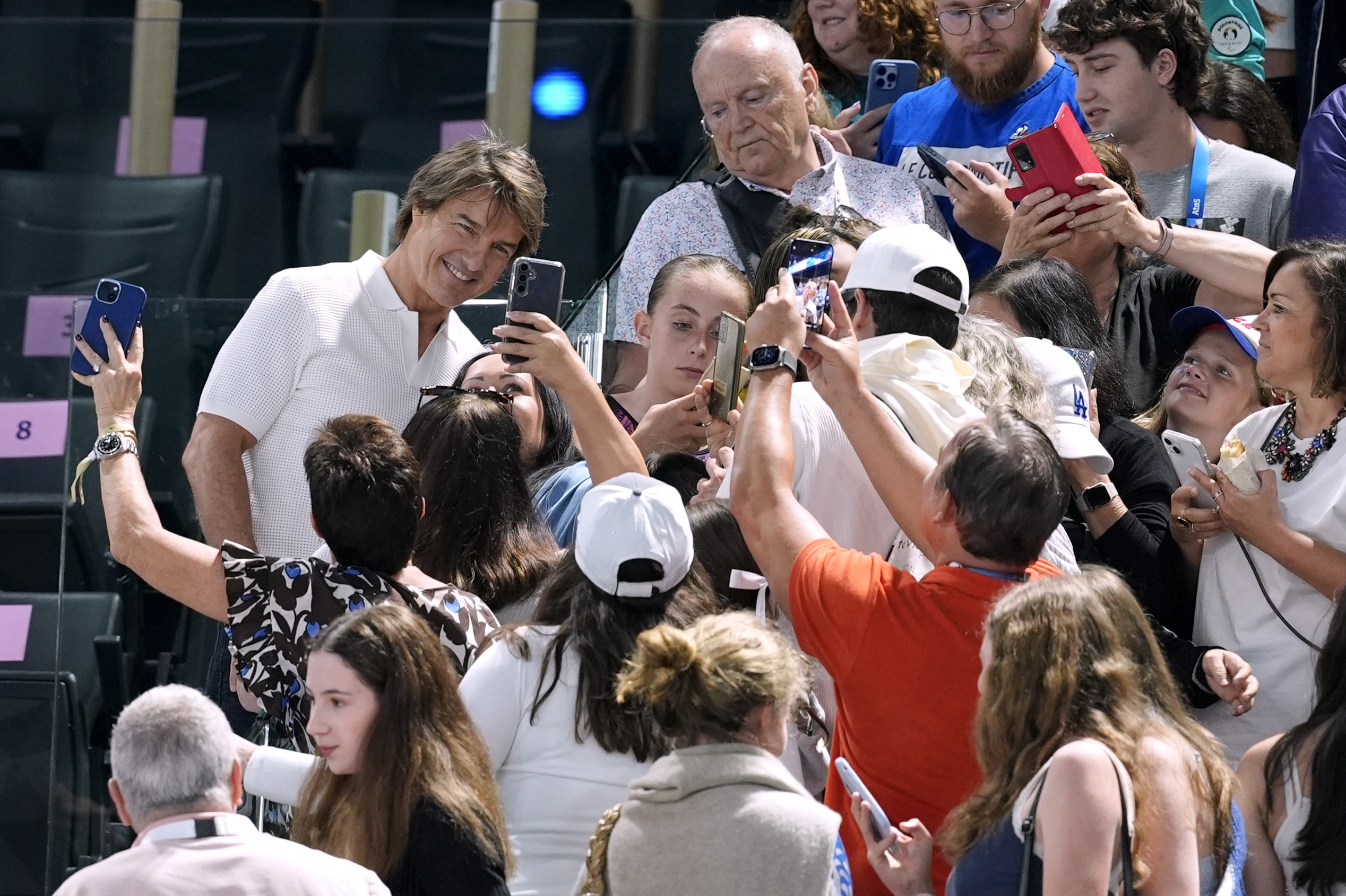 Actor Tom Cruise, left in white, poses for pictures with fans as he attends the women's artistic gymnastics qualification round at the 2024 Summer Olympics