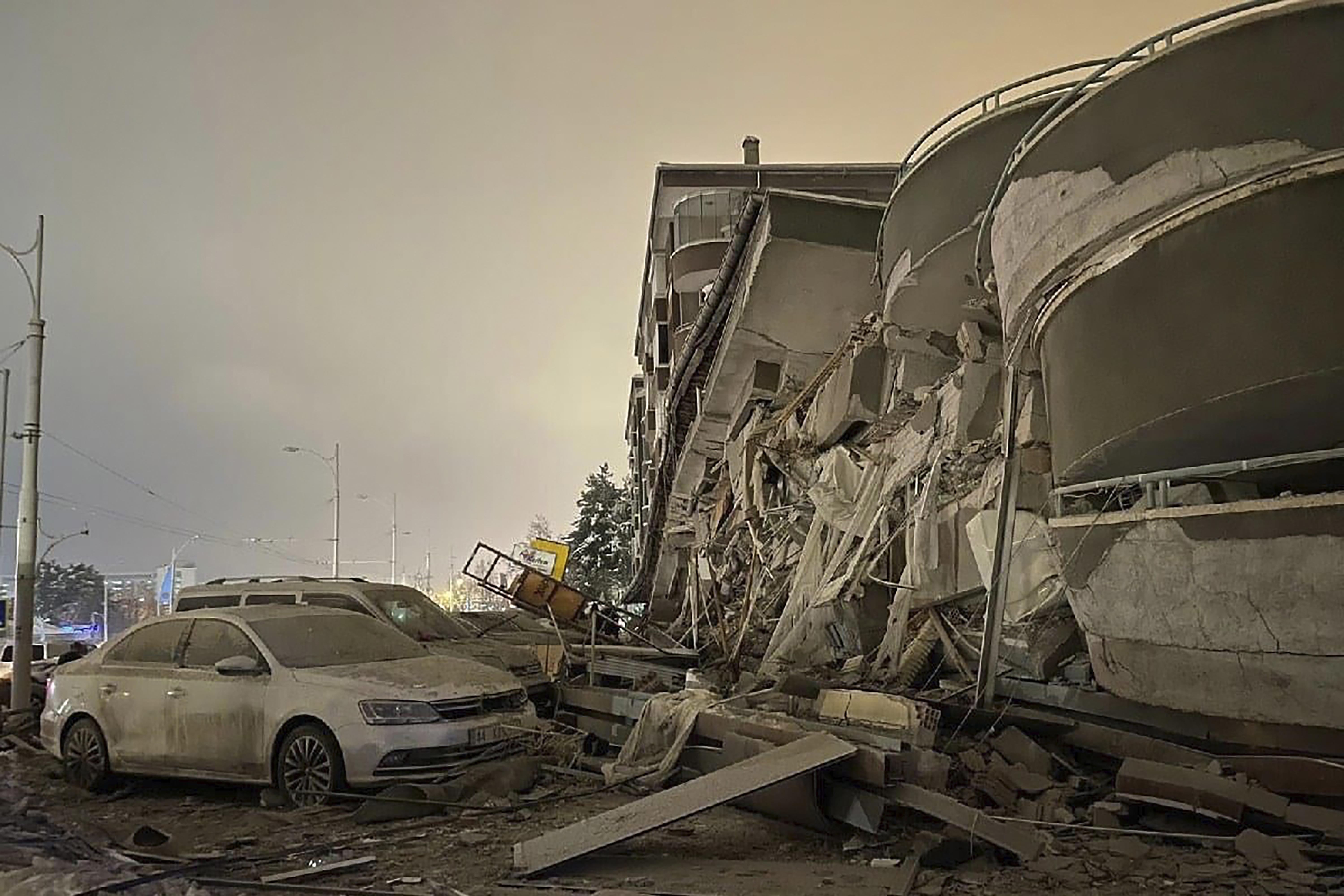 Damaged vehicles sit parked in front of a collapsed building following an earthquake in Diyarbakir, southeastern Turkey, early Monday, Feb. 6, 2023.