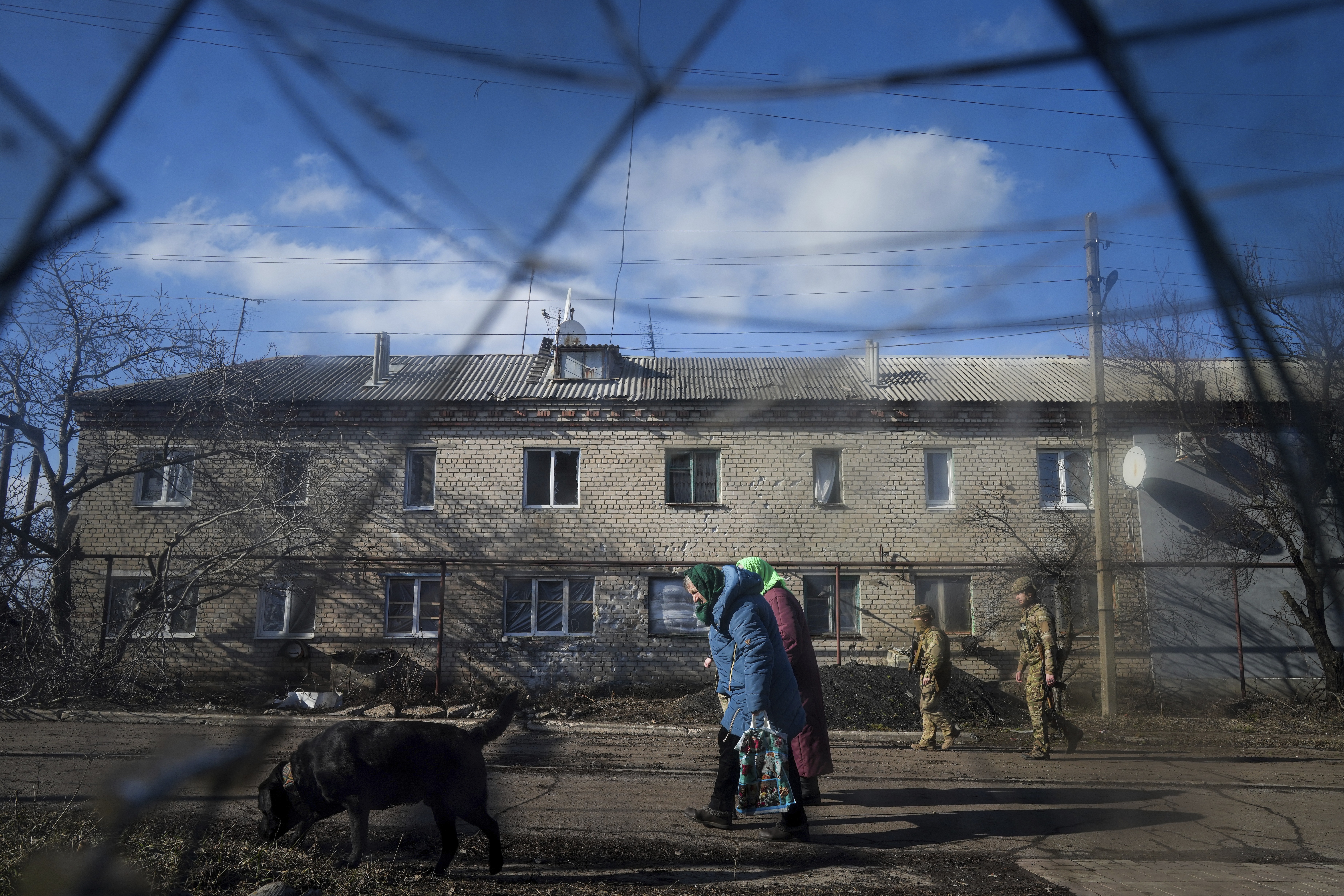 Two Ukrainian soldiers patrol a street as elderly women walk past a house damaged by artillery shelling in Novoluhanske, eastern Ukraine amid the threat of a Russian invasion. 