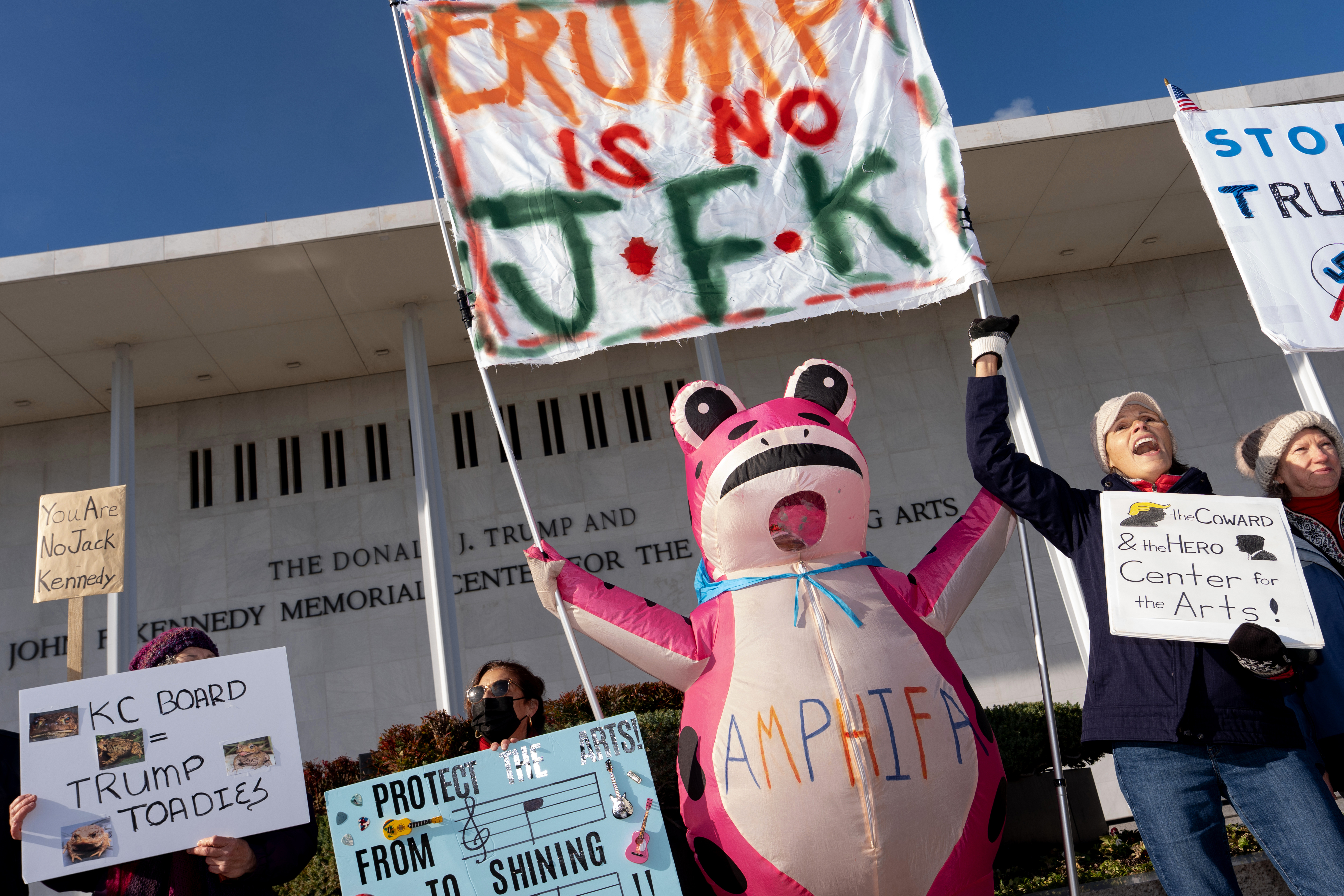 Demonstrators hold up signs at a designated protest point in front of the John F. Kennedy Memorial Centre for the Performing Arts.