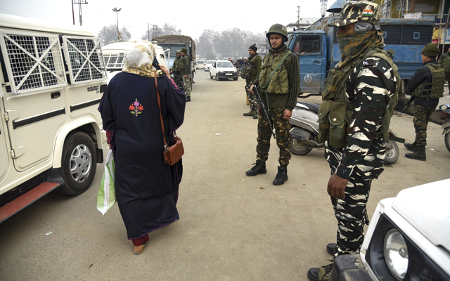 A Kashmiri woman walks past Indian Paramilitary forces standing guard close to the site of a blast in Indian controlled Kashmir. At least three people were wounded in a low-intensity blast in Srinagar city, on November 26.