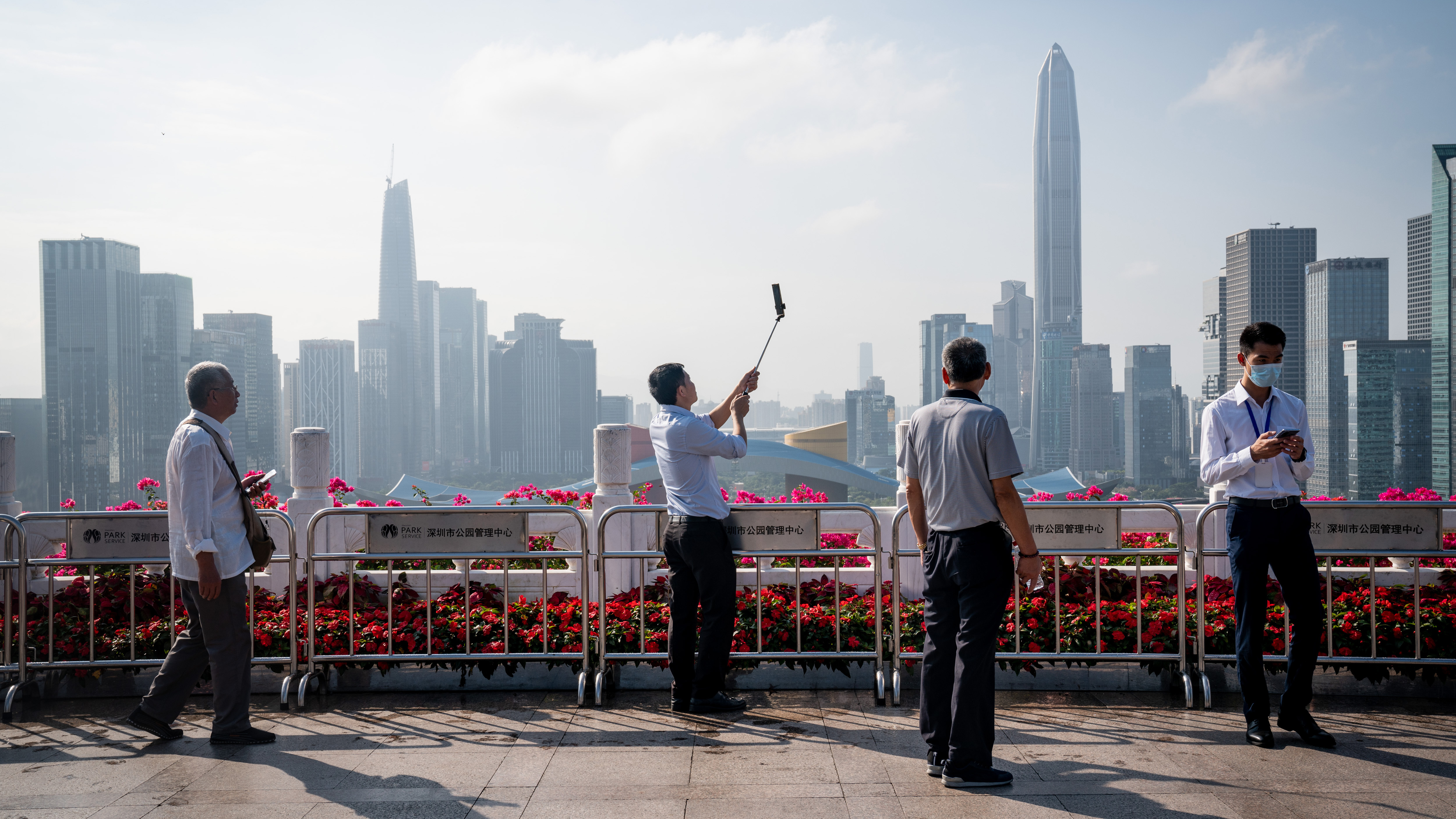 People take photographs against a backdrop of the Shenzhen skyline at Lianhuashan Park in Shenzhen, China