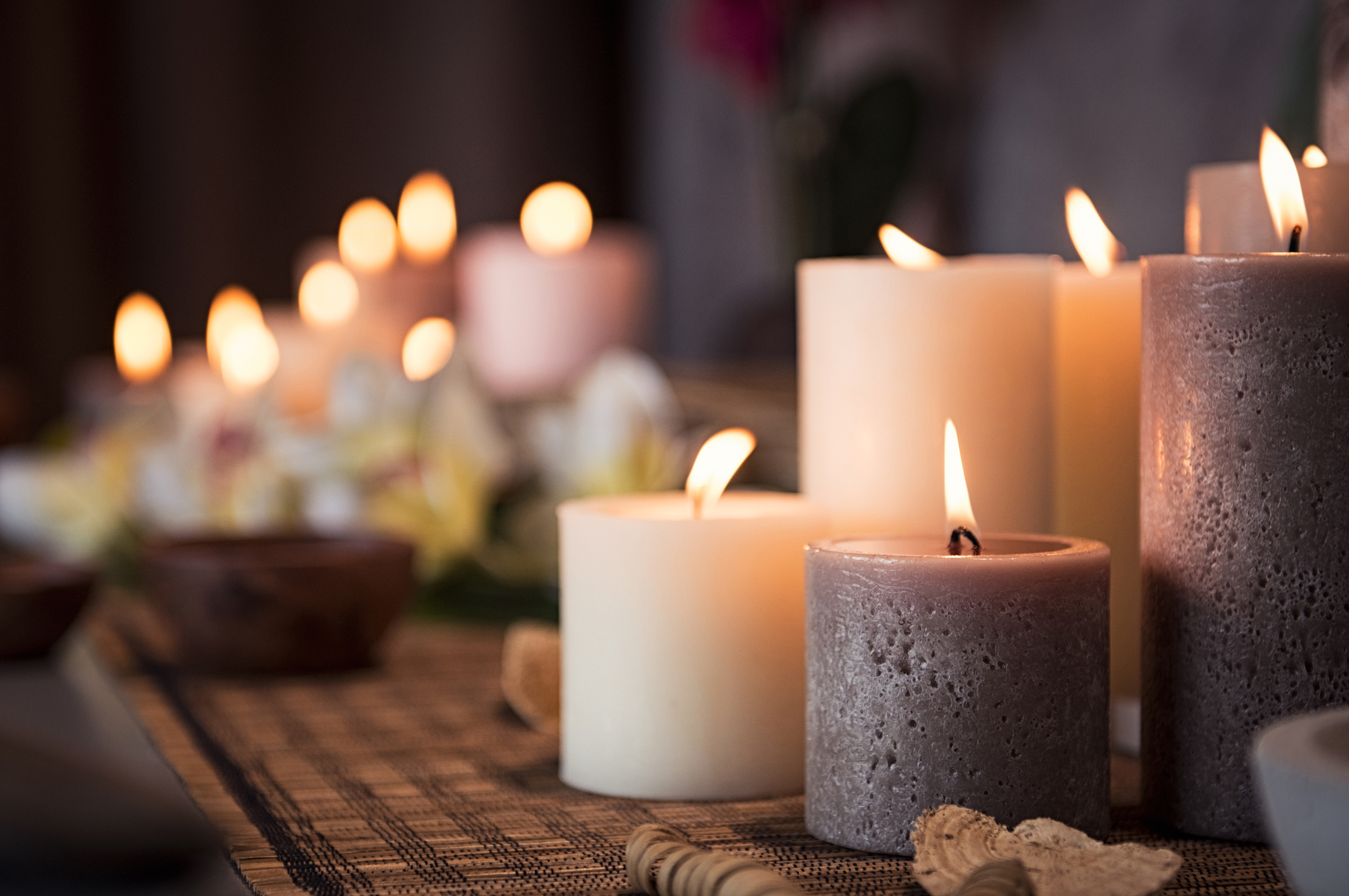 Closeup of burning candles spreading aroma on table in a spa room. Beautiful composition with grey and white candles for spa treatment.