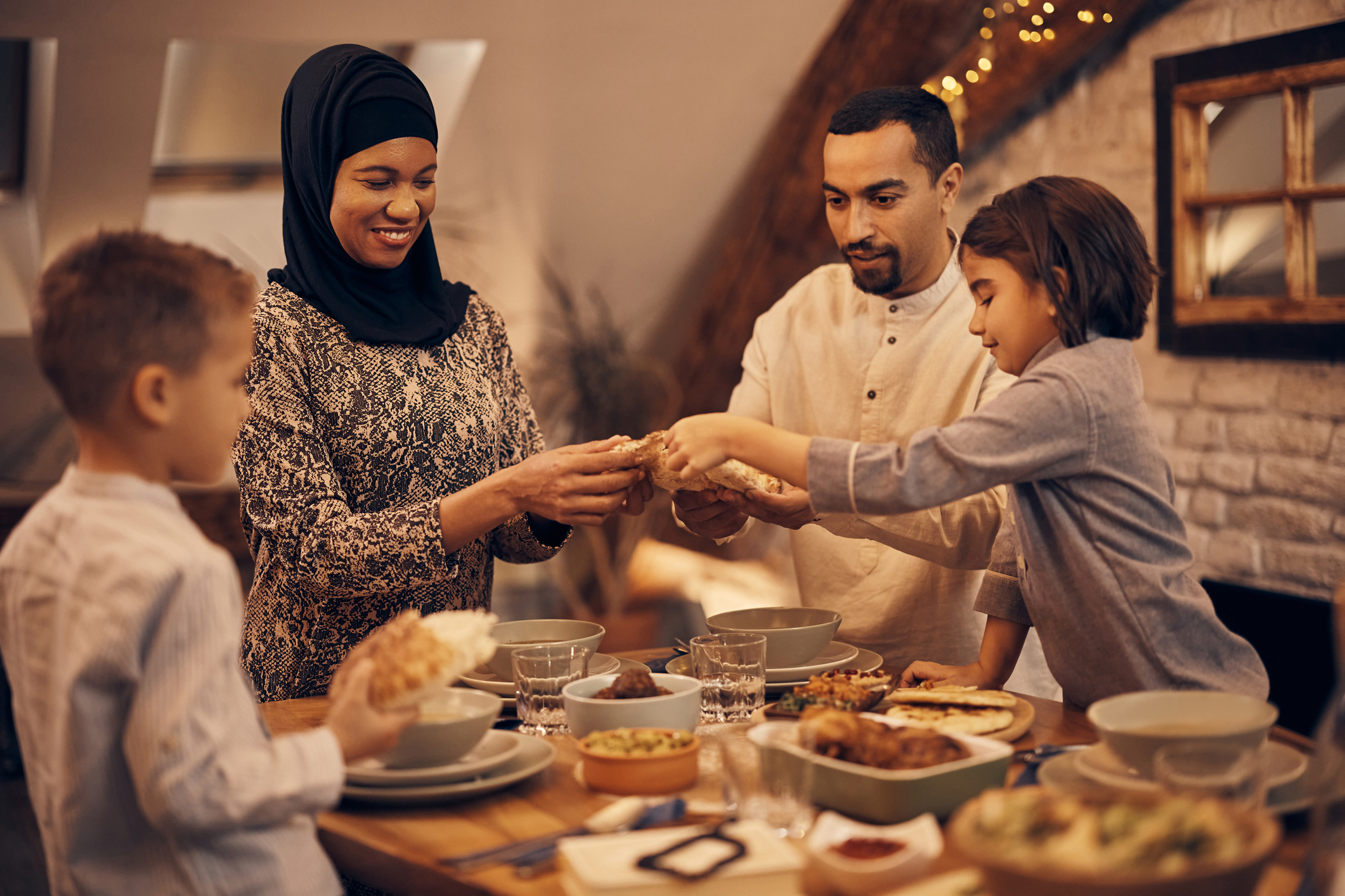 Happy Middle Eastern family sharing pita bread at dining table on Ramadan during iftar.