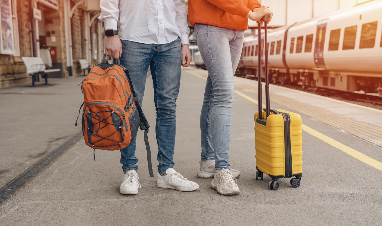 Travelers with a backpack and yellow suitcase waiting for a train at the train station. The couple missed the train. Travel concept.