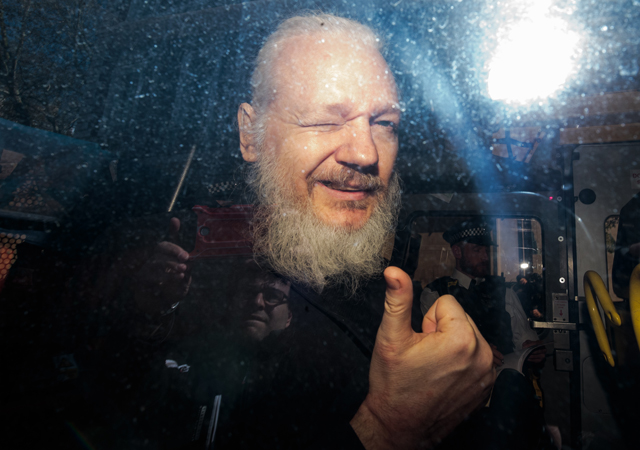 Julian Assange gestures to the media from a police vehicle on his arrival at Westminster Magistrates court on April 11, 2019 in London, England