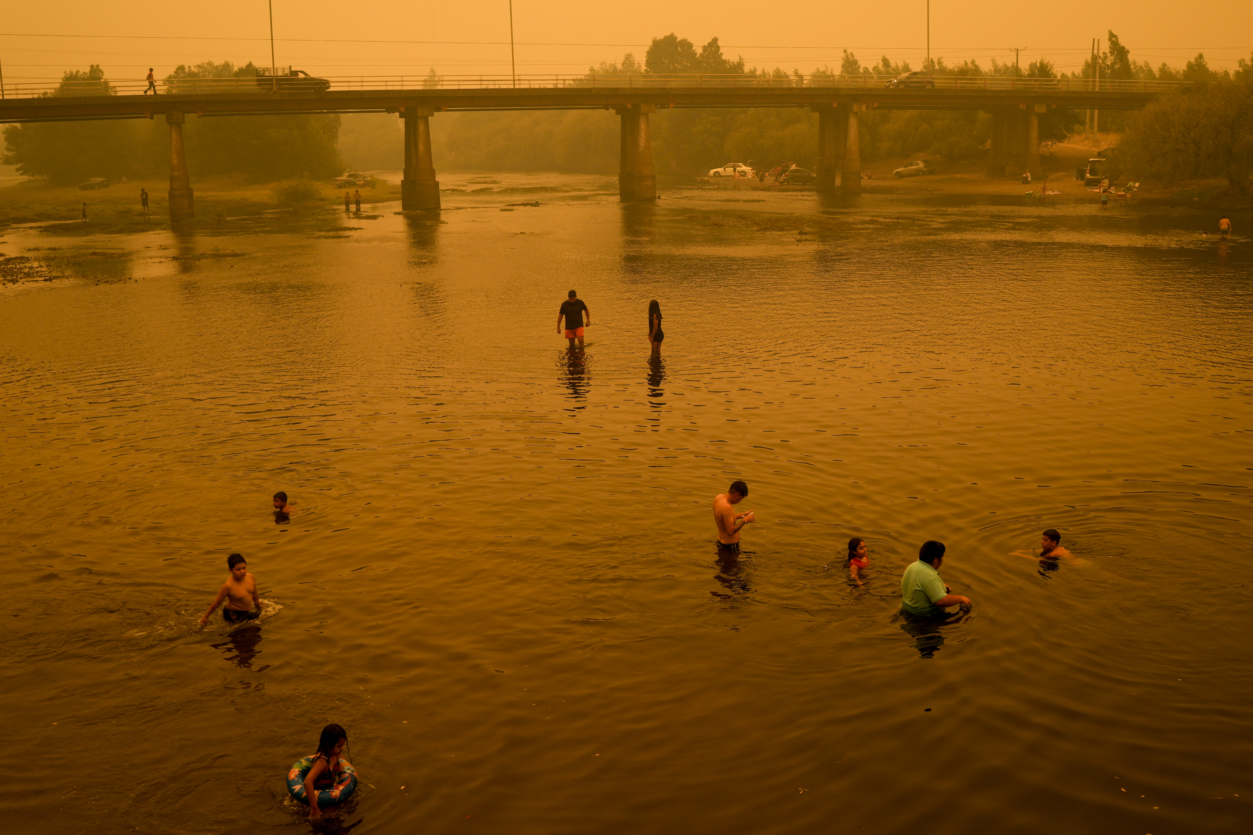 People wade in the river under a smoked-filled sky caused by wildfires, in Renaico Chile, Saturday, Feb. 4, 2023. Wildfires are spreading in southern and central Chile, triggering evacuations and the declaration of a state of emergency in some regions. 