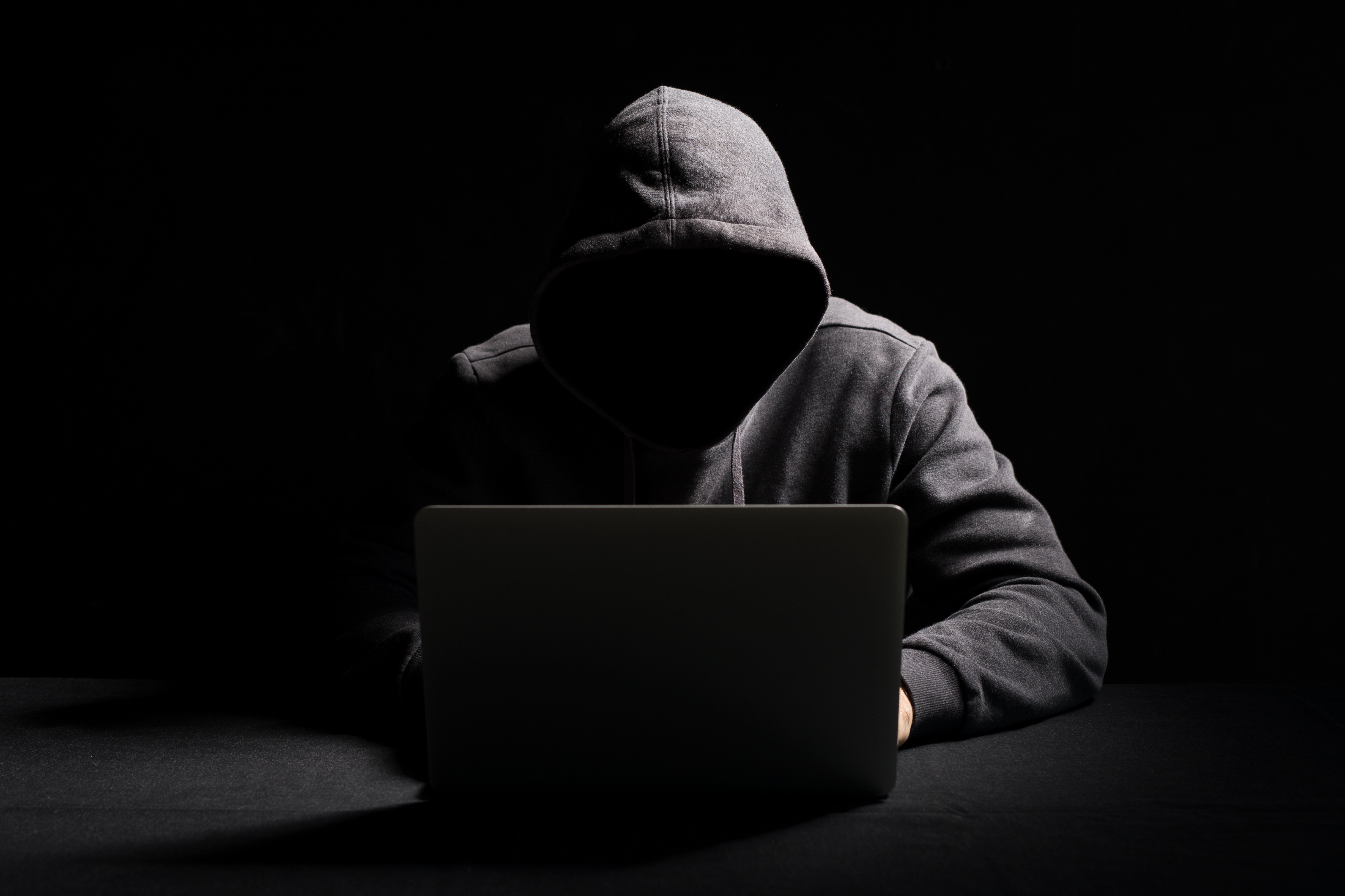 Hacker working on laptop in the dark - scam - shadowy figure online