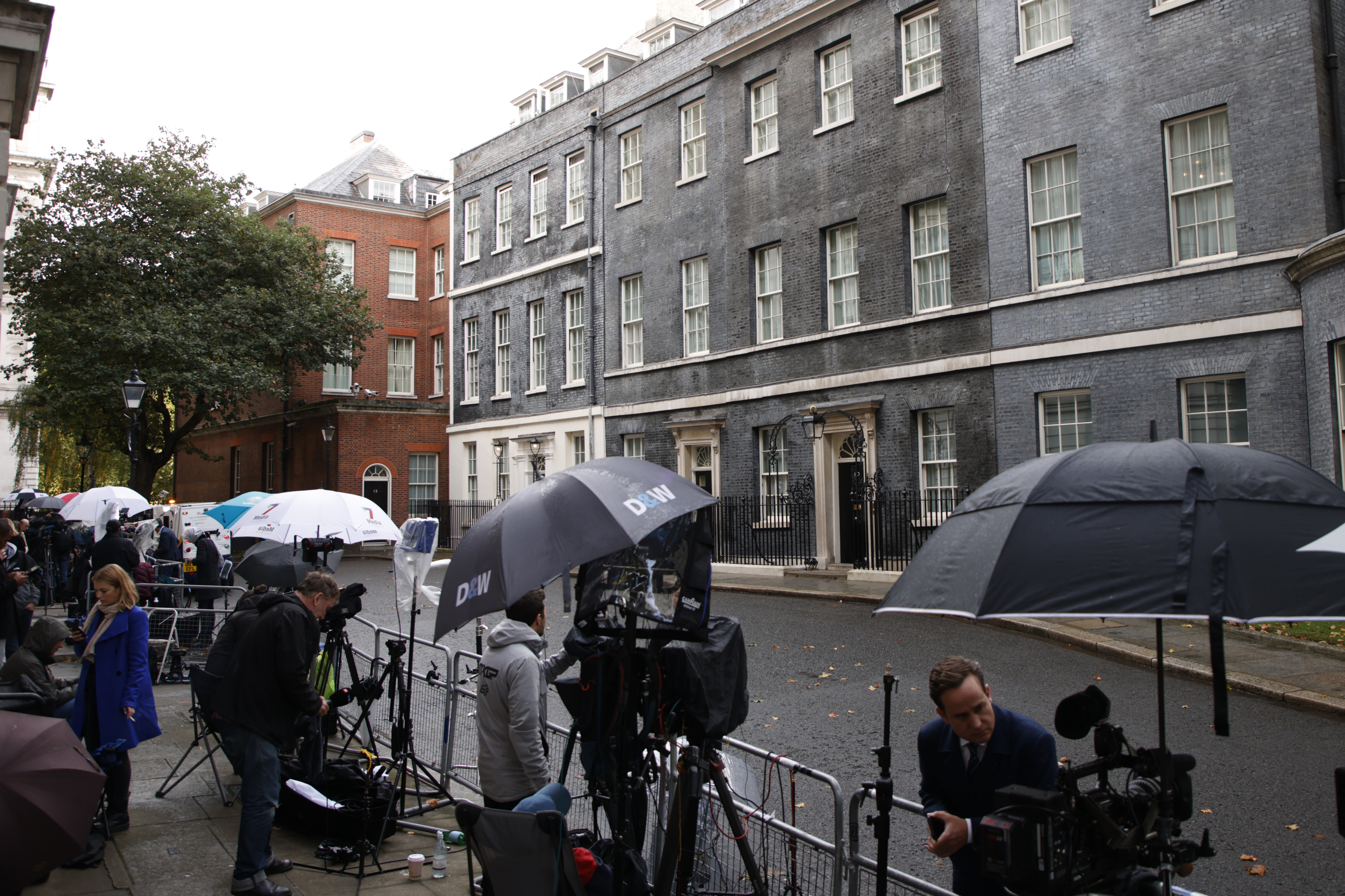 Media take shelter underneath umbrellas as they wait outside 10 Downing Street the official home of the British Prime Minister in London, Friday, Oct. 21, 2022. 