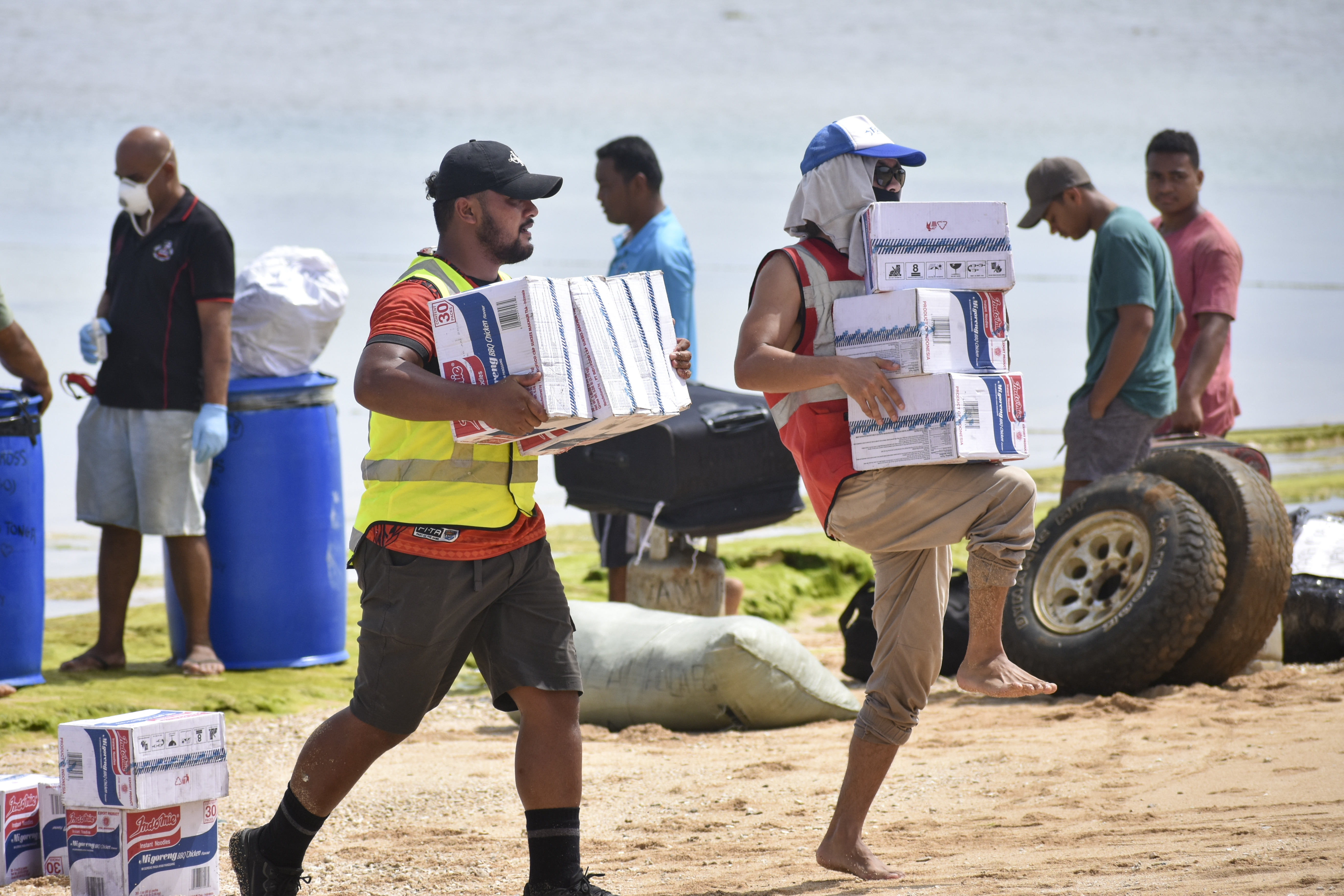 In this photo provided by Malau Media/IFRC, Tonga Red Cross Society's staff and volunteers unloading boxes of noodles from the boat into the beach in Nomuka on Ha'apai Island, Tonga on April 1, 2022. Three months on from a devastating volcano and tsunami in Tonga, the AP checks in on how the island nation is recovering. The bill from the tsunami is estimated at some $90 million and GDP is expected to fall by more than 7% this year. The cleanup has been hindered by an internet outage caused by th