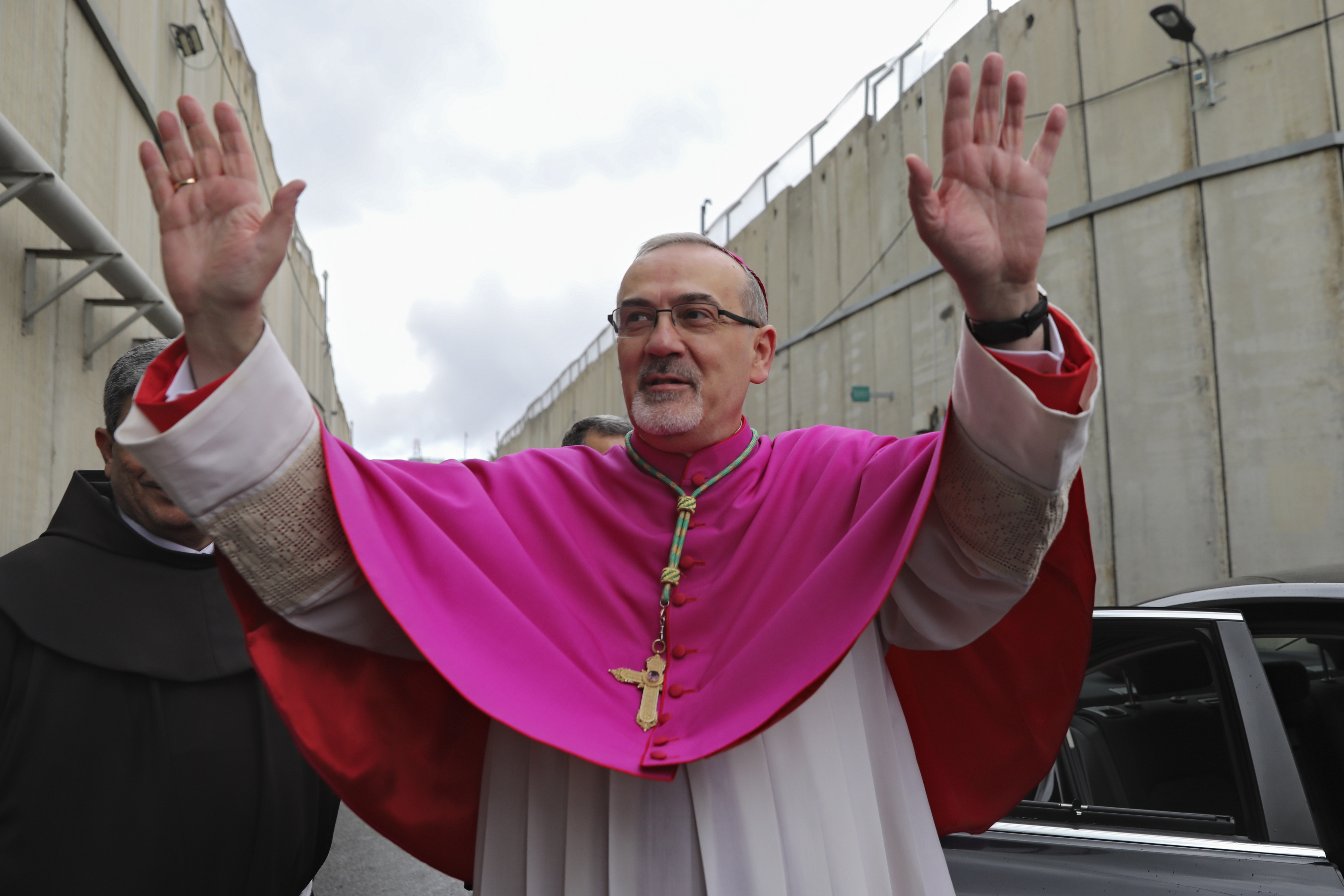 Latin Patriarch Pierbattista Pizzaballa greets worshippers next to the separation wall between the West Bank city of Bethlehem and Jerusalem on his way to the Church of the Nativity in Bethlehem, Friday, Dec. 24, 2021. 
