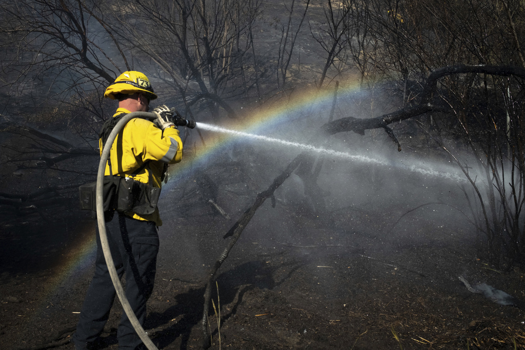 Un bombero limpia con manguera los puntos calientes del incendio Archer en la sección Granada Hills de Los Ángeles.