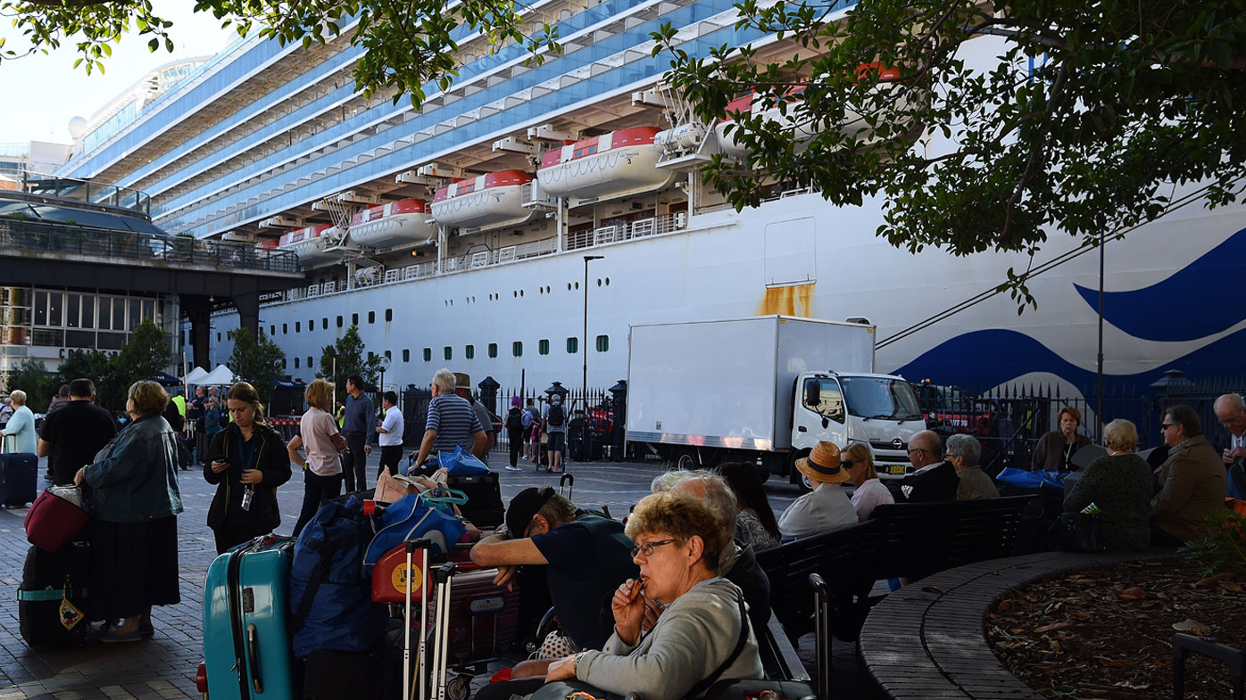 Passengers sit with their luggage after disembarking from the Ruby Princess cruise ship at the Overseas Passenger Terminal in Circular Quay, Sydney.
