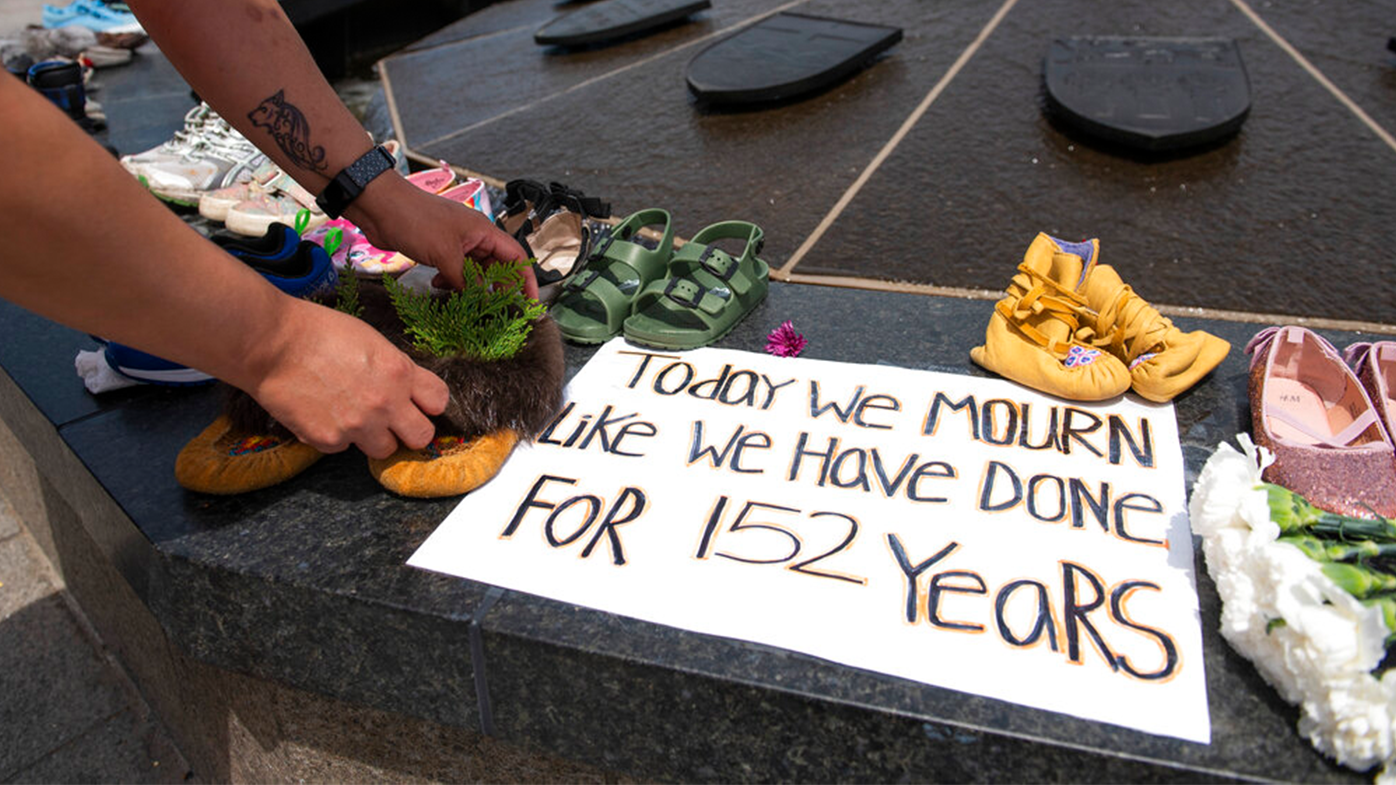 Stephanie Gilpin, whose parents, aunts and uncles were sent to residential schools, smooths out the cedar that she placed in a pair of moccasins at the Centennial Flame on Parliament Hill in Ottawa, Ontario, in memory of the 215 children whose remains were found at the grounds of the former Kamloops Indian Residential School on Sunday, May 30, 2021.