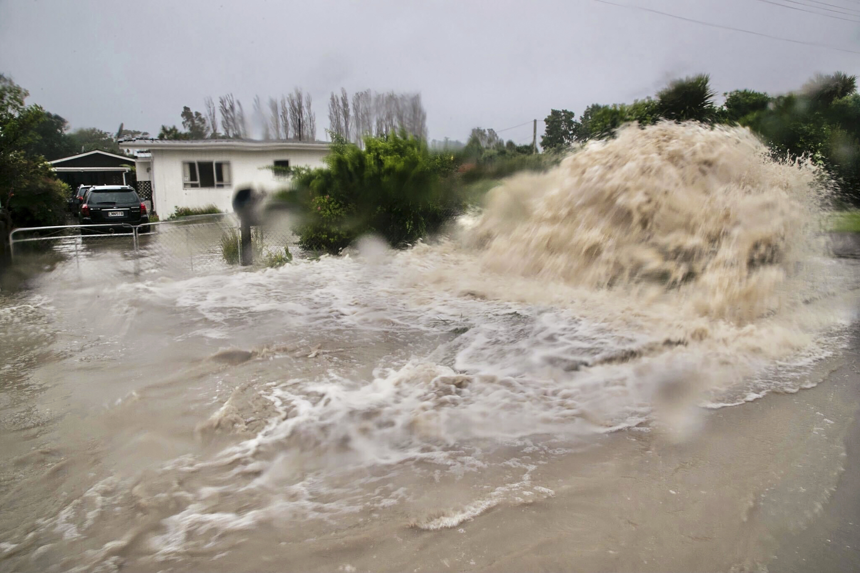 Water gushes from a storm drain access port on a street in Te Awanga, southeast of Auckland, New Zealand, Tuesday, Feb. 14, 2023.  