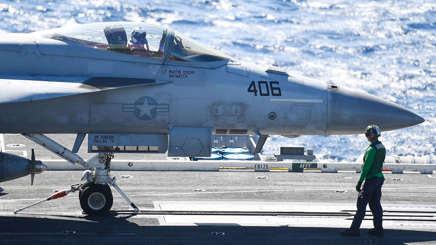 Un miembro de la tripulación de camisa verde 'Hook Runner' mueve un Super Hornet a su posición antes del lanzamiento