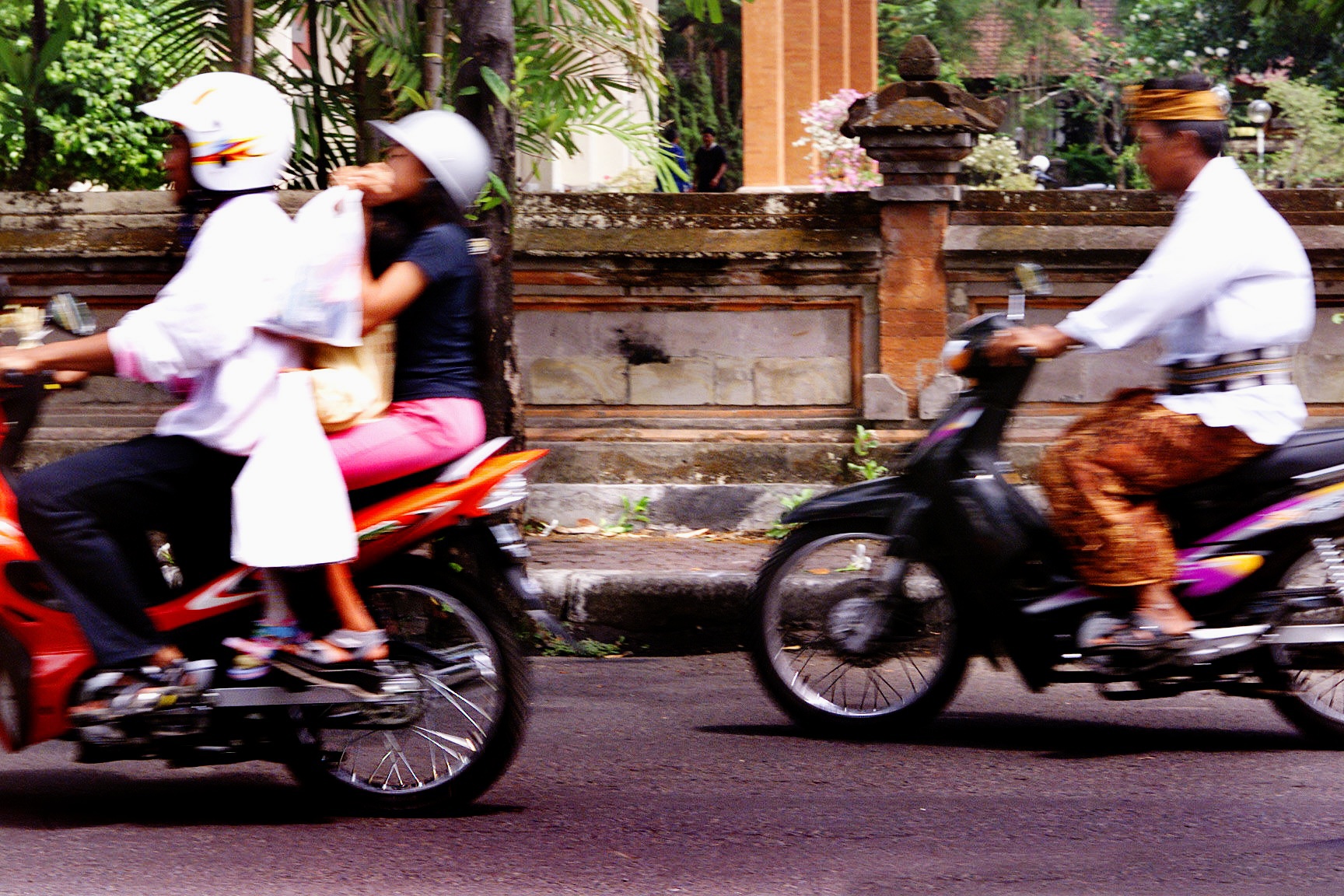 DIGICAM 00000000 SMH,NEWS,Grenade. Motorbikes drive past the Denpasar Court House where a plastic bag containing a grenade and AK47 bullets was dumped on the footpath of the sidewall in the early hours of this morning, today 21st November.2002.Denpasar, Bali. the bag was dumped inbetween the 2 bikes below the black mark on the wall with flower on right . Picture by KATE GERAGHTY/klg