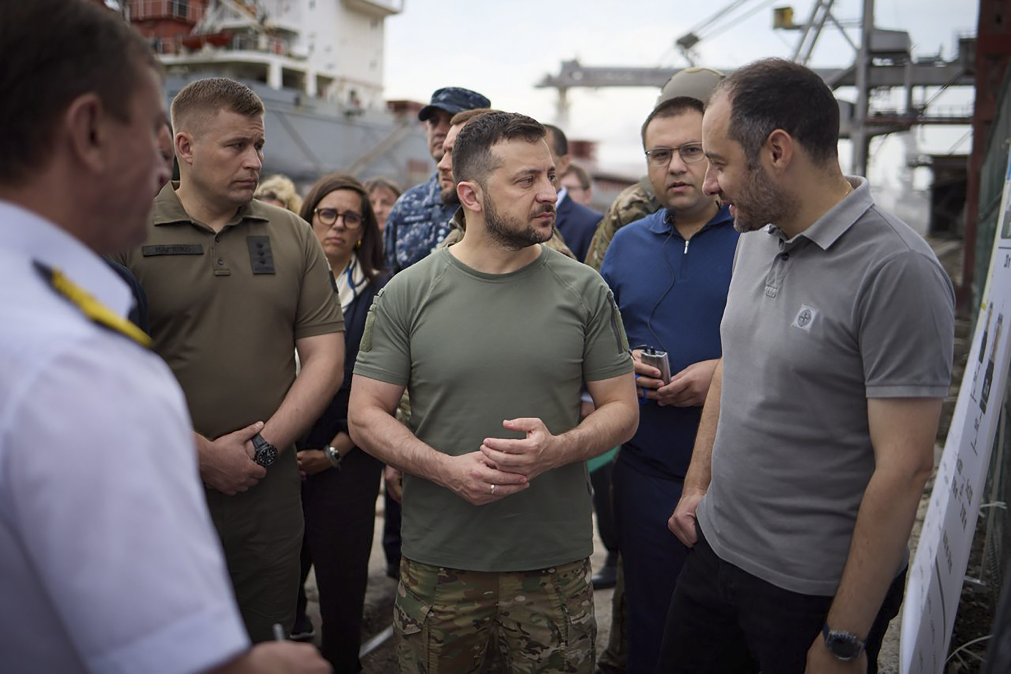 In this photo provided by the Ukrainian Presidential Press Office, Ukrainian President Volodymyr Zelenskyy, center, surrounded by ambassadors of different countries and UN officials, visits a port in Chornomork during loading of grain on a Turkish ship, background, close to Odesa, Ukraine, Friday, July 29, 2022. (Ukrainian Presidential Press Office via AP)