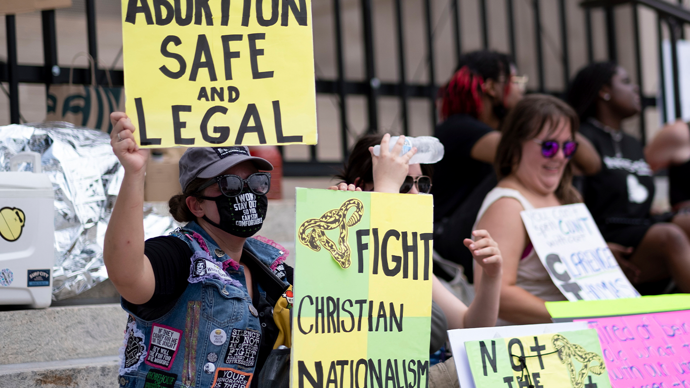 Un pequeño grupo se sienta en los escalones del Capitolio del Estado de Georgia para protestar por la revocación de Roe v. Wade el domingo 26 de junio de 2022. (AP Photo/Ben Gray)