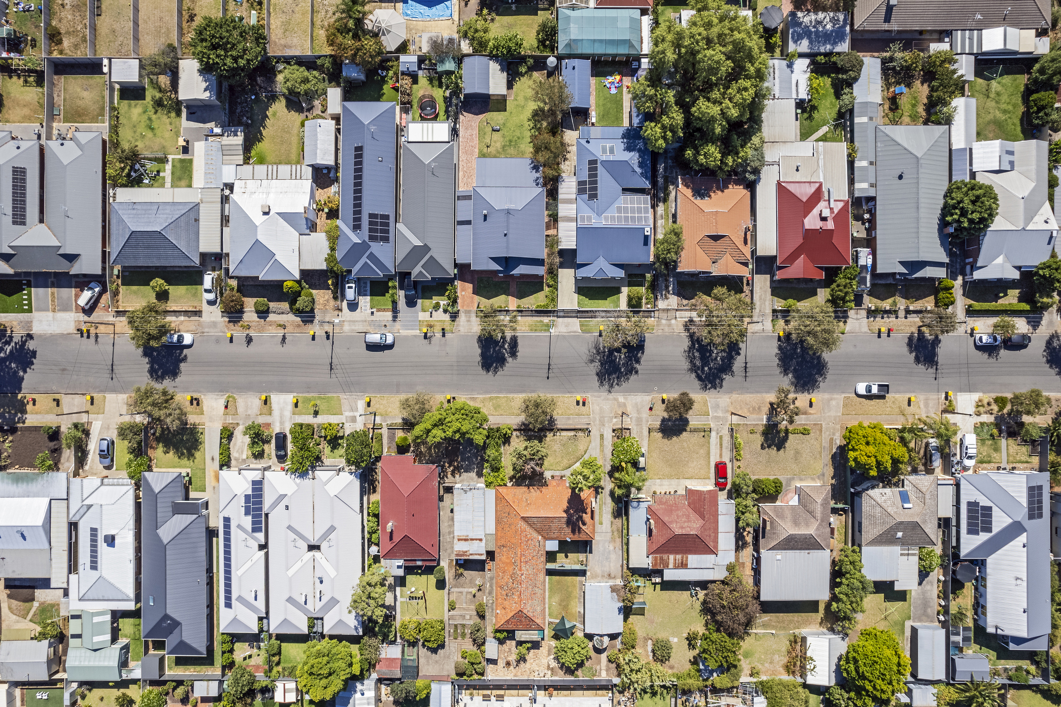 Aerial view directly above established houses in older Adelaide southern suburb: looking down on front & back yards some landscaped, one with construction work. Yellow & red topped wheeled garbage (rubbish) bins are parked on kerbside awaiting collection. Powerlines run down the street for the houses. Cars parked on the street and in private properties.