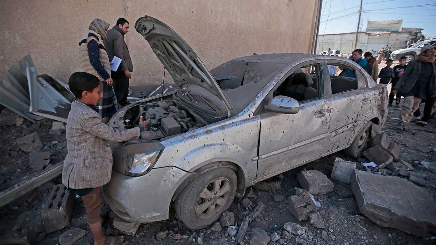 People inspect a damaged car at the site of airstrikes by a Saudi-led coalition on a workshop, in Sanaa, Yemen.