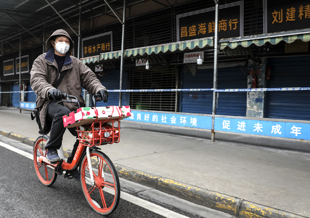 A man wears a mask while riding on mobike past the closed Huanan Seafood Wholesale Market, which has been linked to cases of coronavirus.