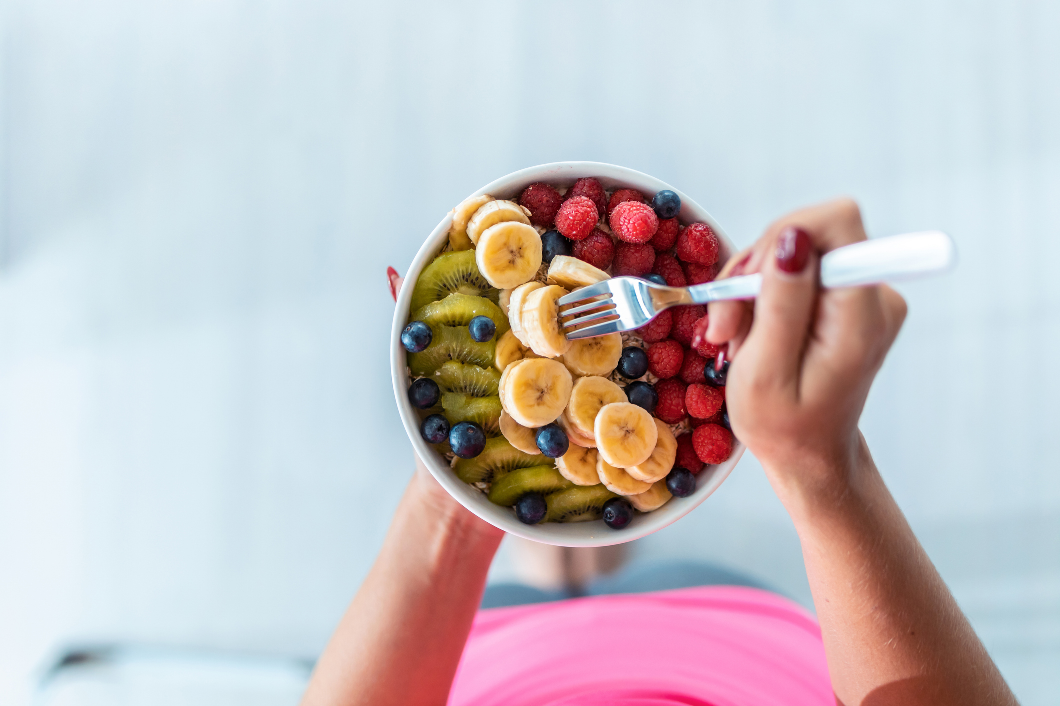 Close-up of woman's hands holding a bowl with fresh fruit while standing at home.