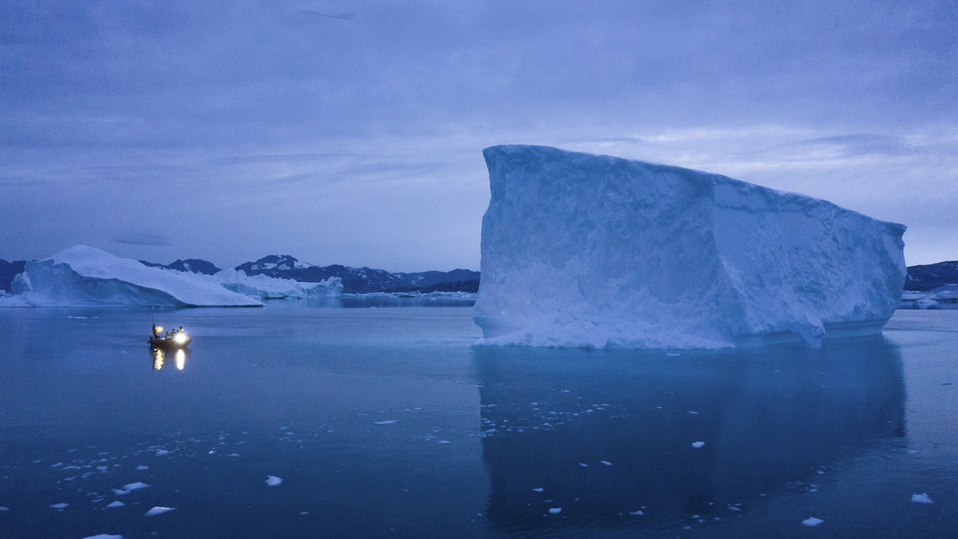 A boat navigates at night next to icebergs in eastern Greenland.