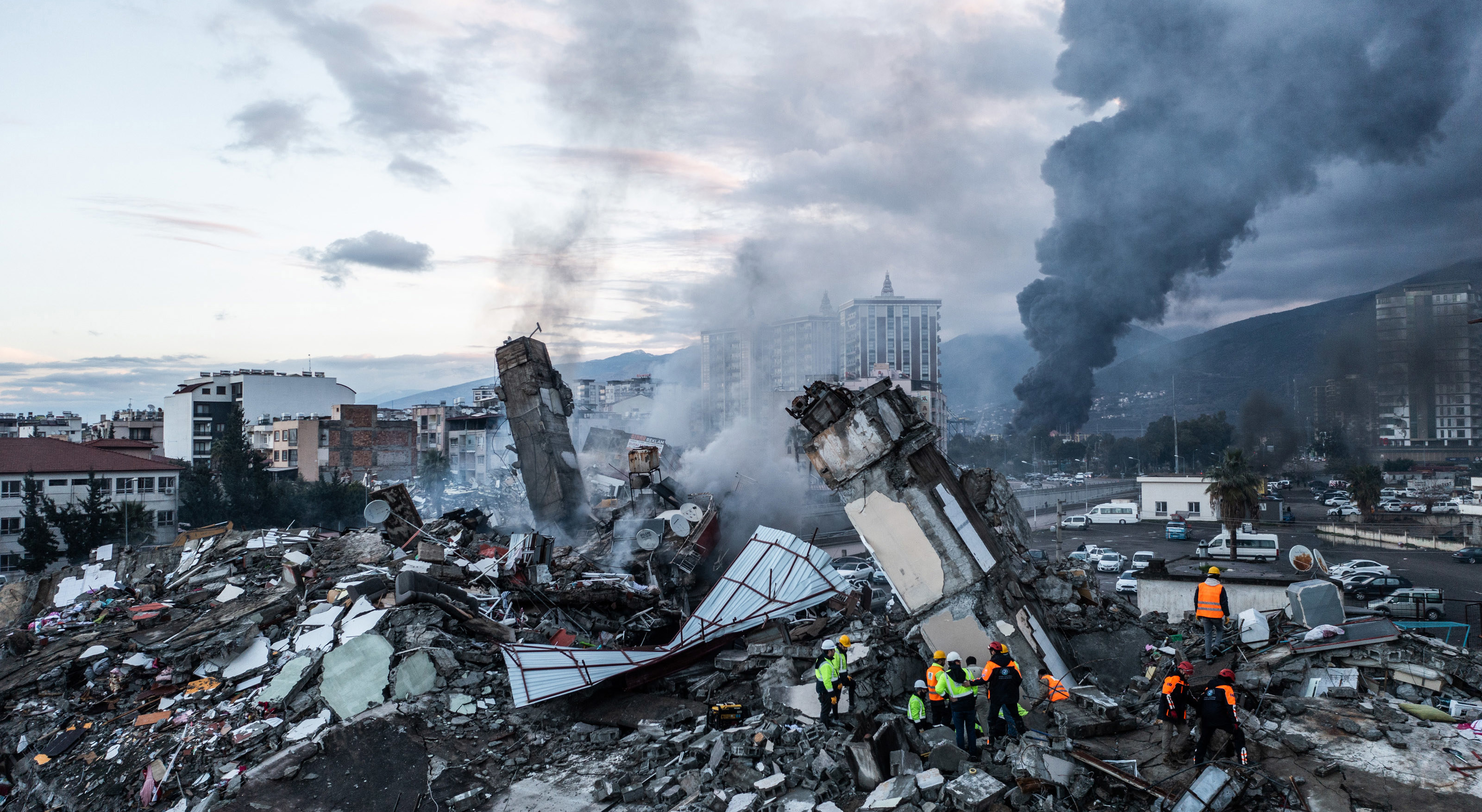 Smoke billows from the Iskenderun Port as rescue workers work at the scene of a collapsed building.