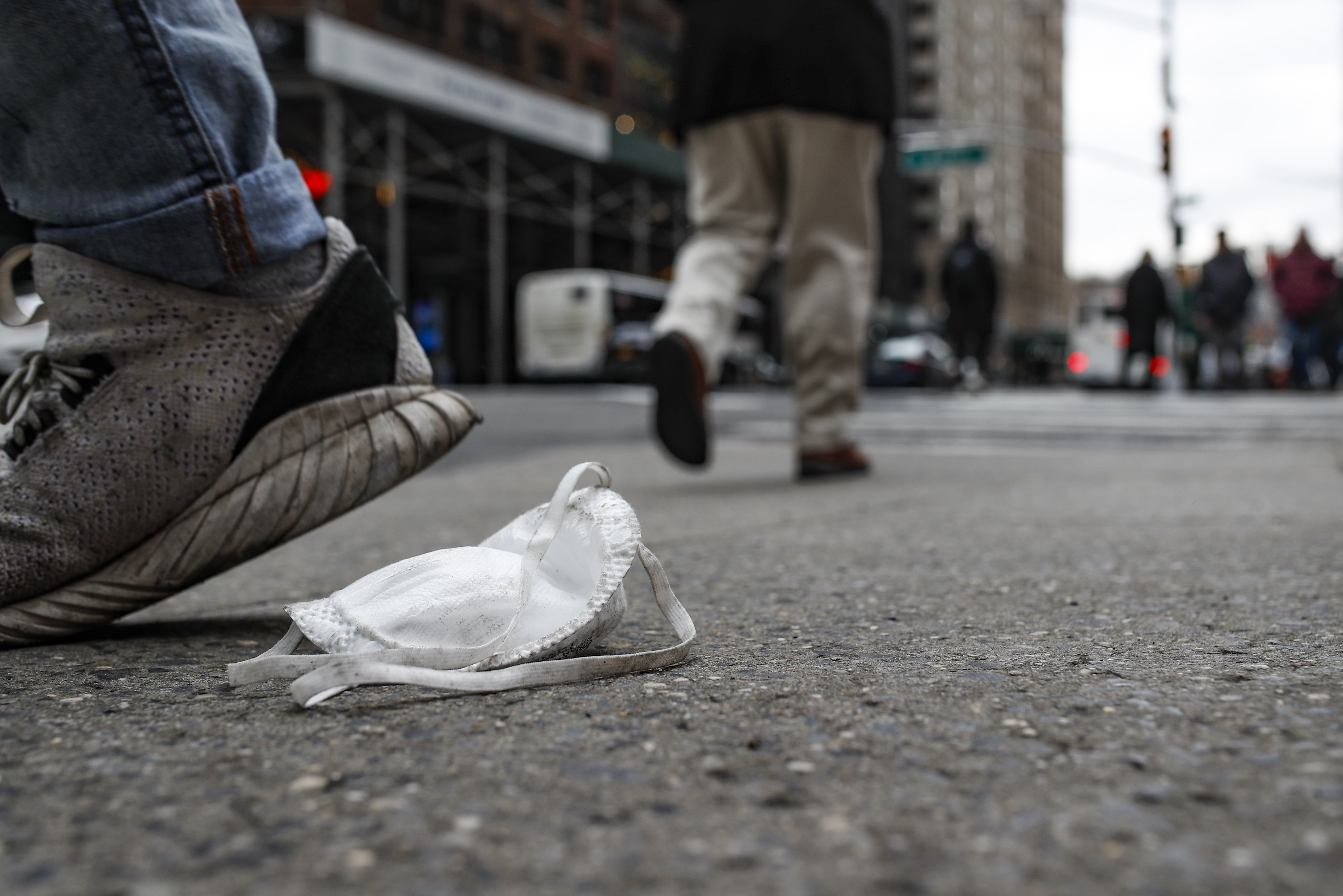 A used protective face mask rests on the pavement as pedestrians pass, Tuesday, March 17, 2020, in New York. 