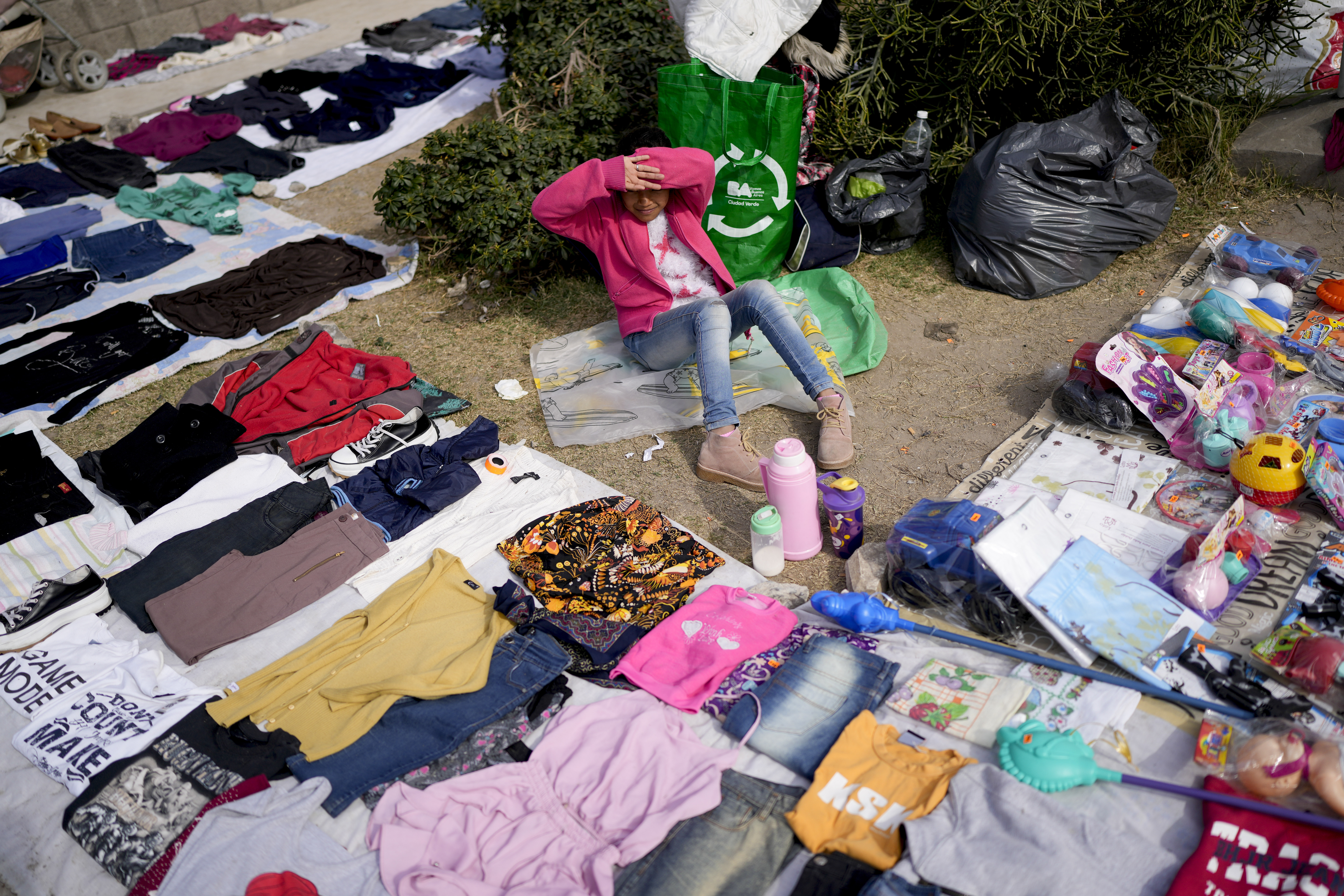 A vendor sits surrounded by her secondhand garments displayed at a market where people can buy or barter goods on the outskirts of Buenos Aires, Argentina.