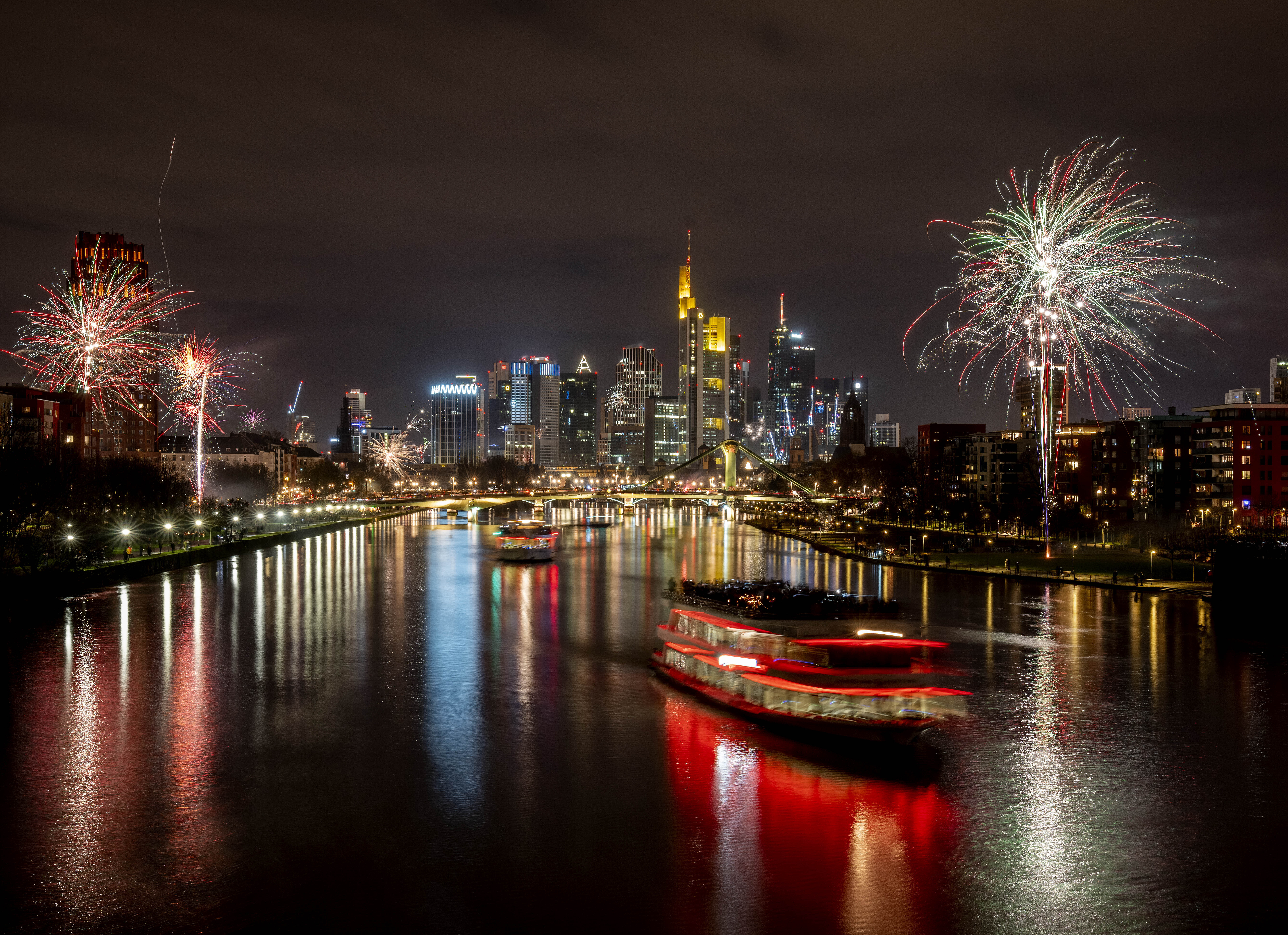 Party boats cruise over the river Main with only a few fireworks near the buildings of the banking district in Frankfurt, Germany, early Saturday, Jan. 1, 2022. 