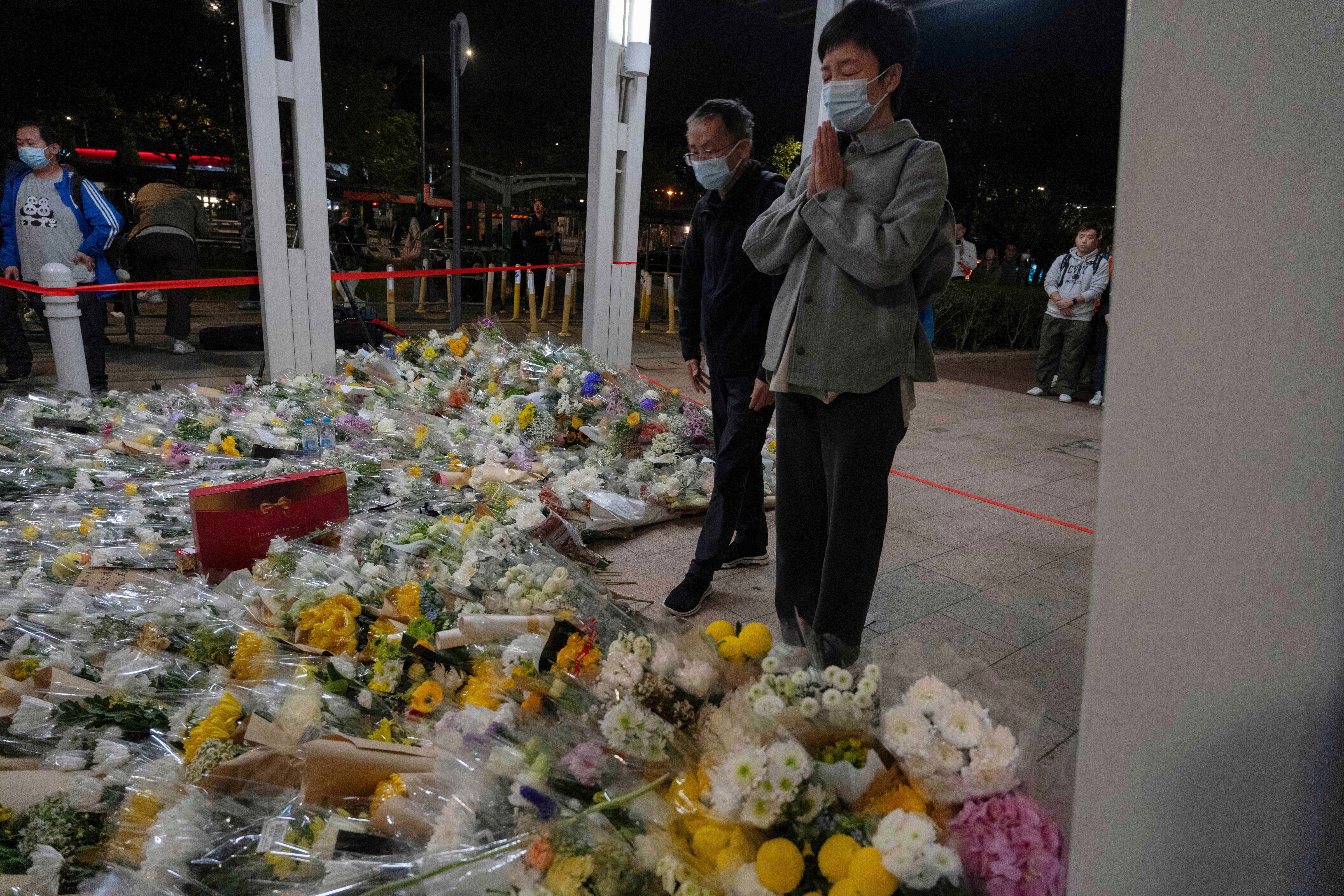 A woman prays after placing flowers near the site of the deadly fire at Wang Fuk Court, a residential estate in the Tai Po district of Hong Kong's New Territories.